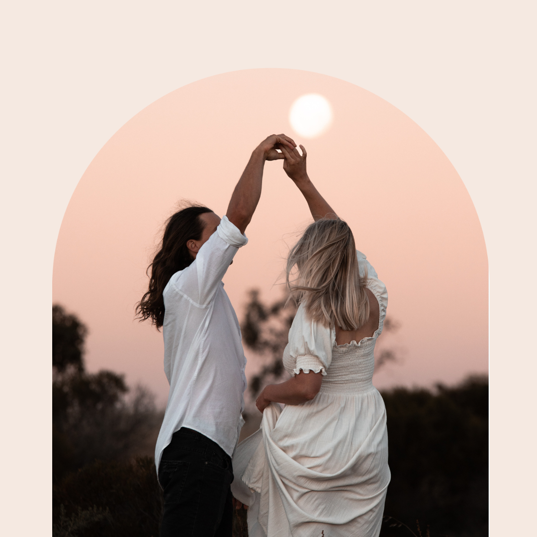 Two people dancing together outdoors at sunset with a soft peachy sky backdrop, creating a romantic silhouette.