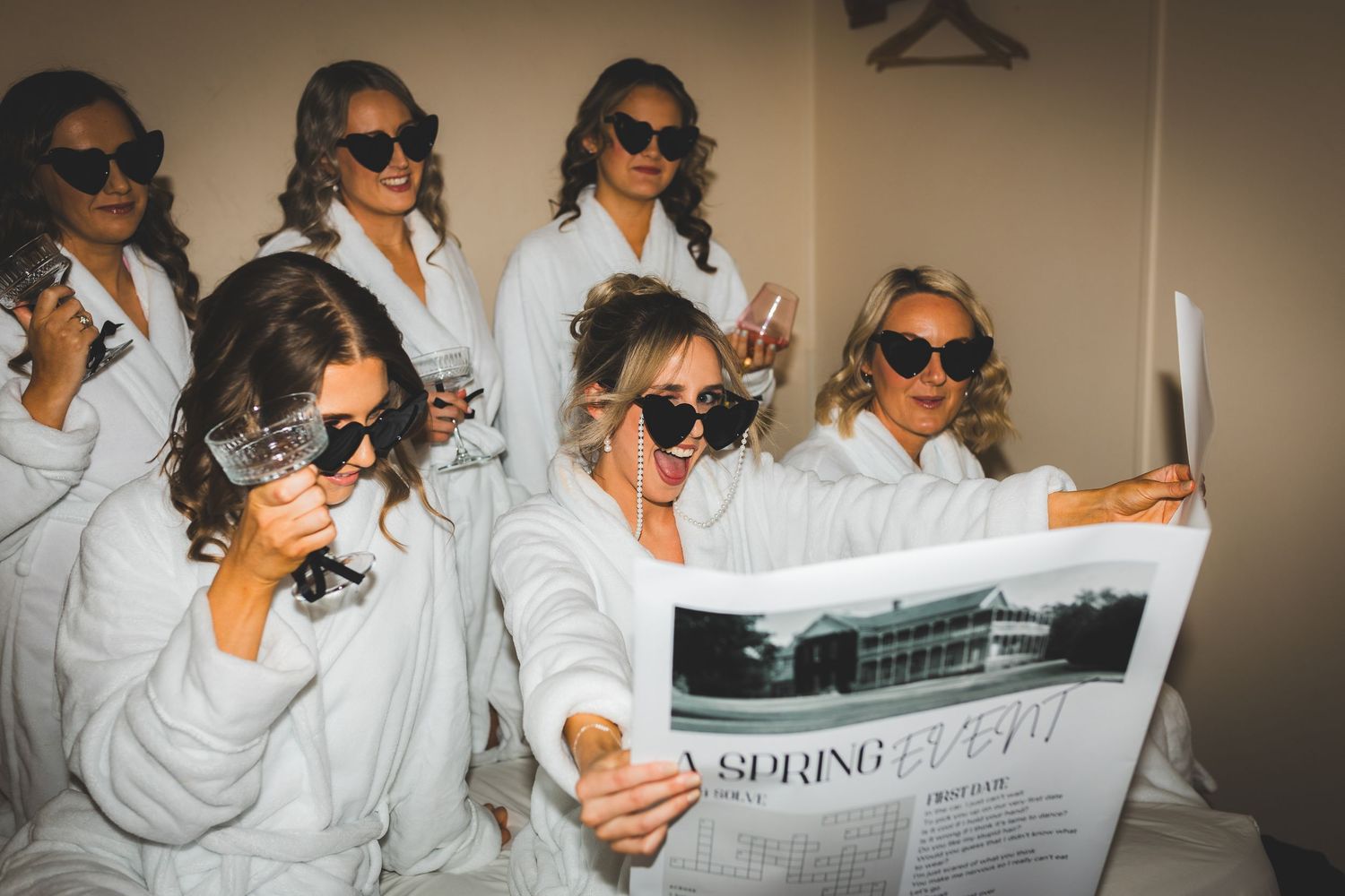 Wedding party in matching white robes and sunglasses read a newspaper while getting ready.