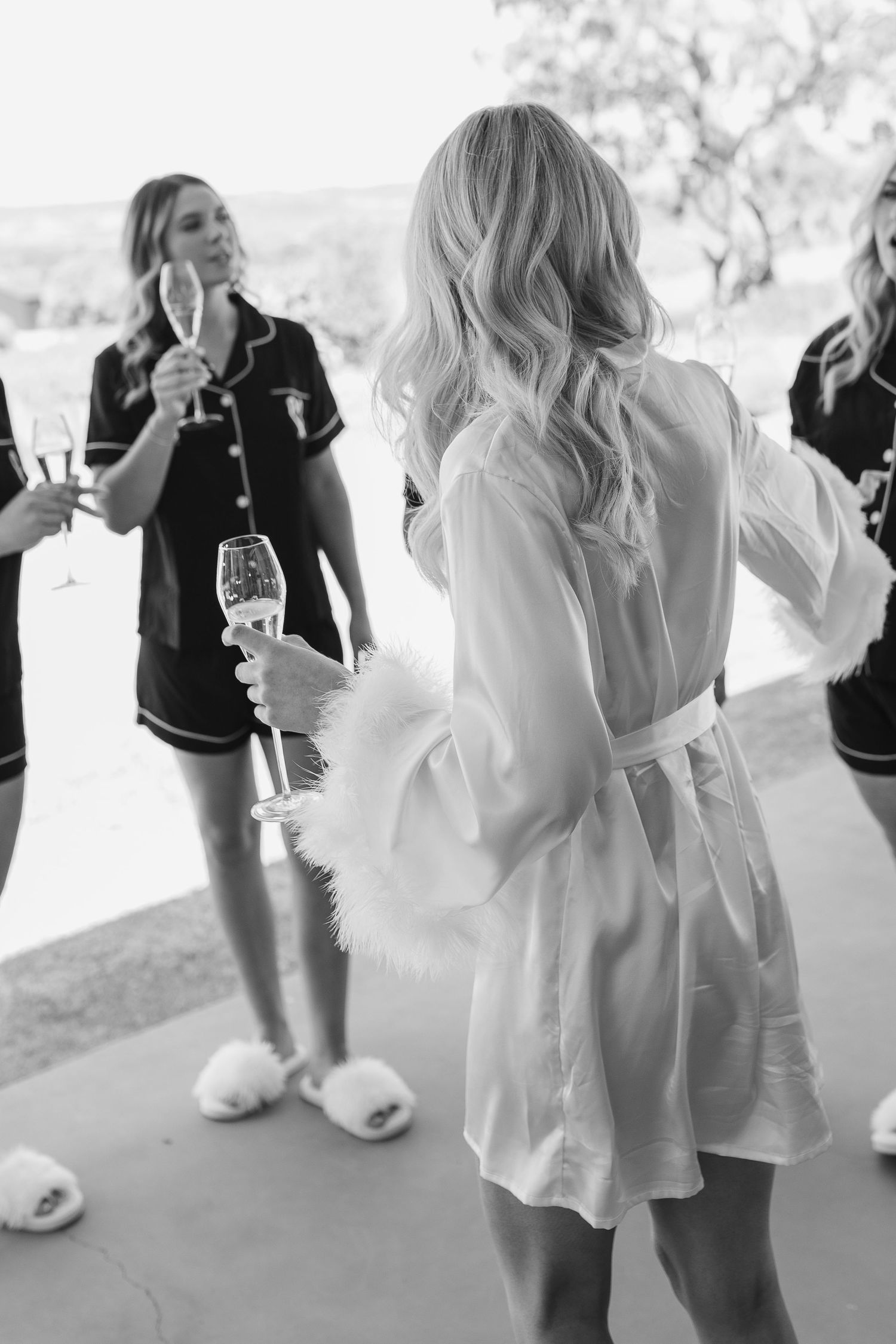 Women in robes celebrating with champagne during wedding preparations.