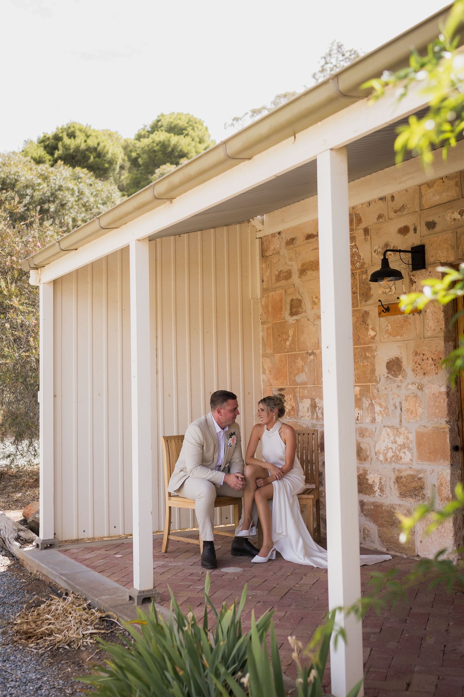 Couple shares tender moment on rustic stone porch with white columns and brick pavers at sunset.