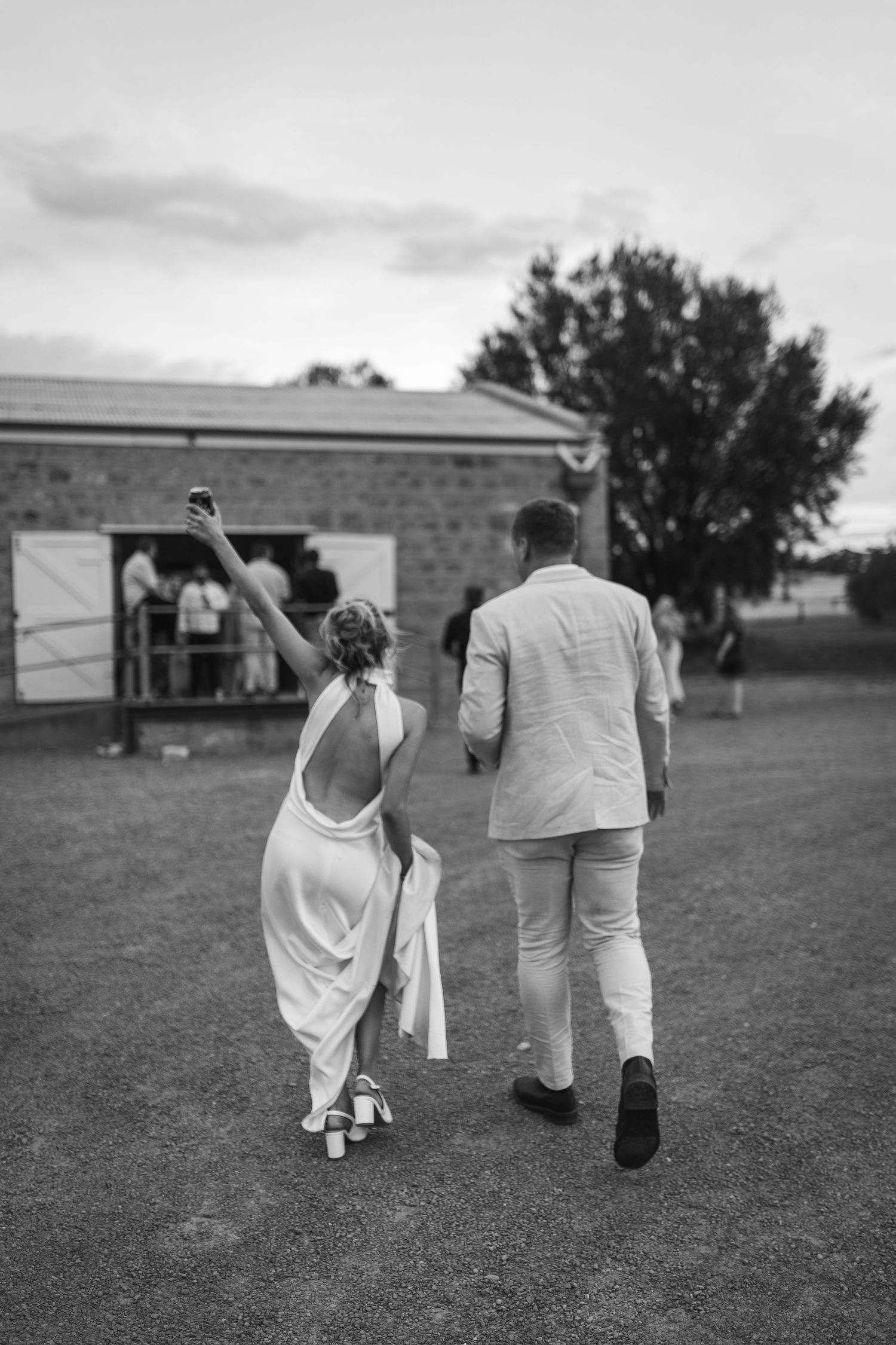 Wedding couple walking away on grass with bride raising arm in celebration.