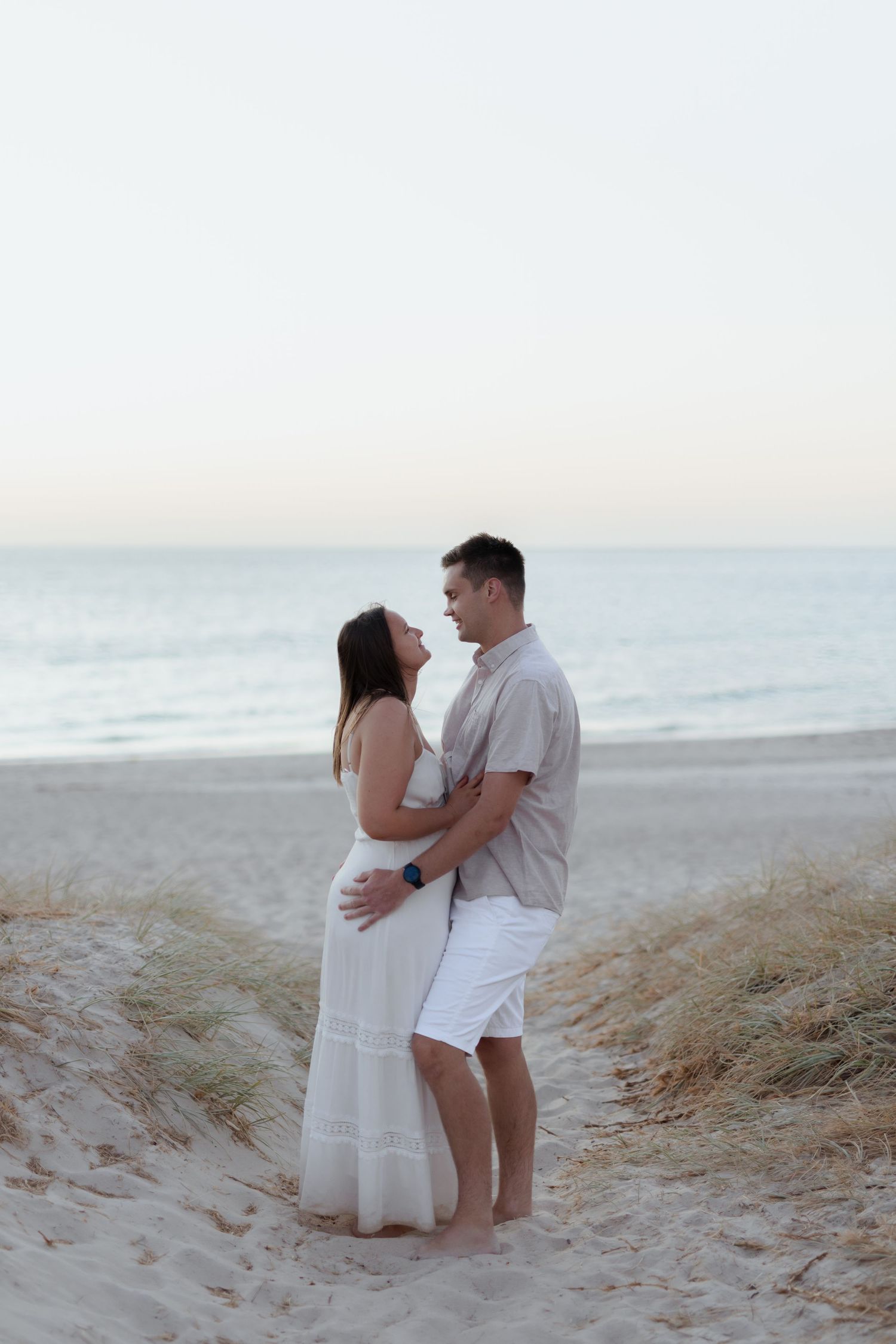 Couple embracing on a beach in white summer clothing.