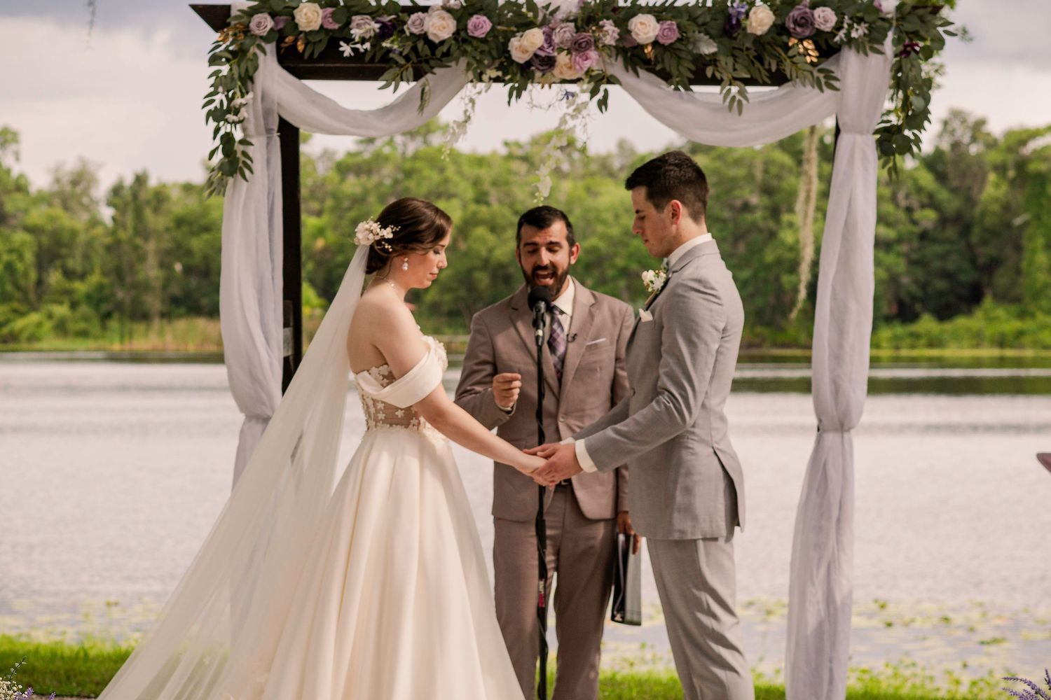 A romantic outdoor wedding ceremony under a floral arch by a serene lake.
