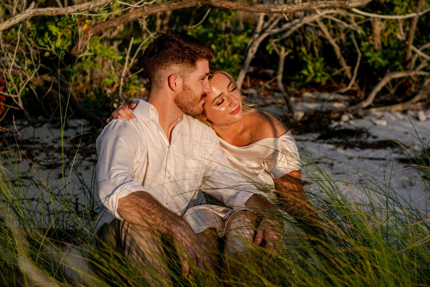 Romantic moment between couple sitting in coastal grass during sunset.