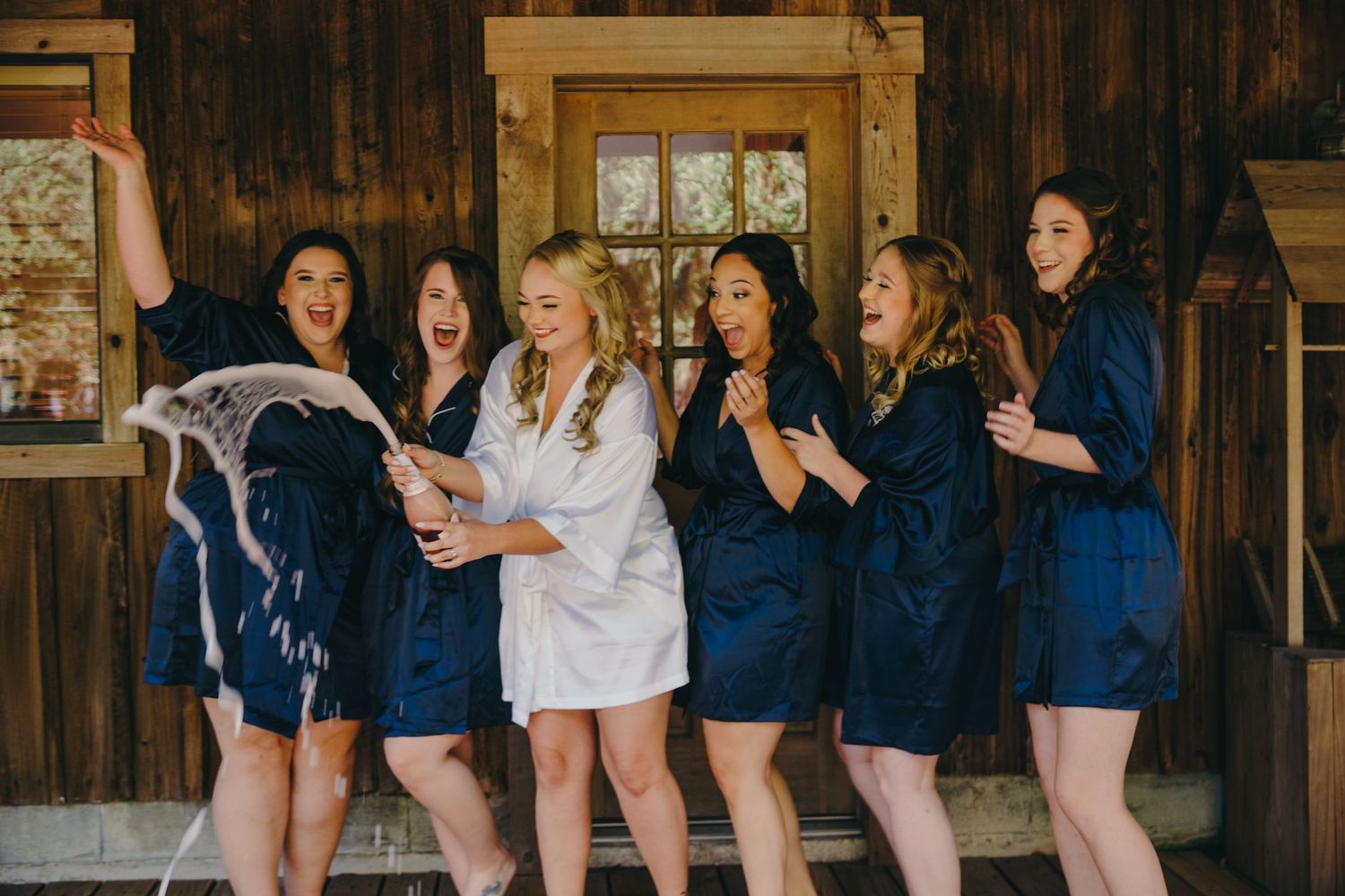 A group in matching navy blue robes share a joyful moment together in a rustic wooden cabin setting.
