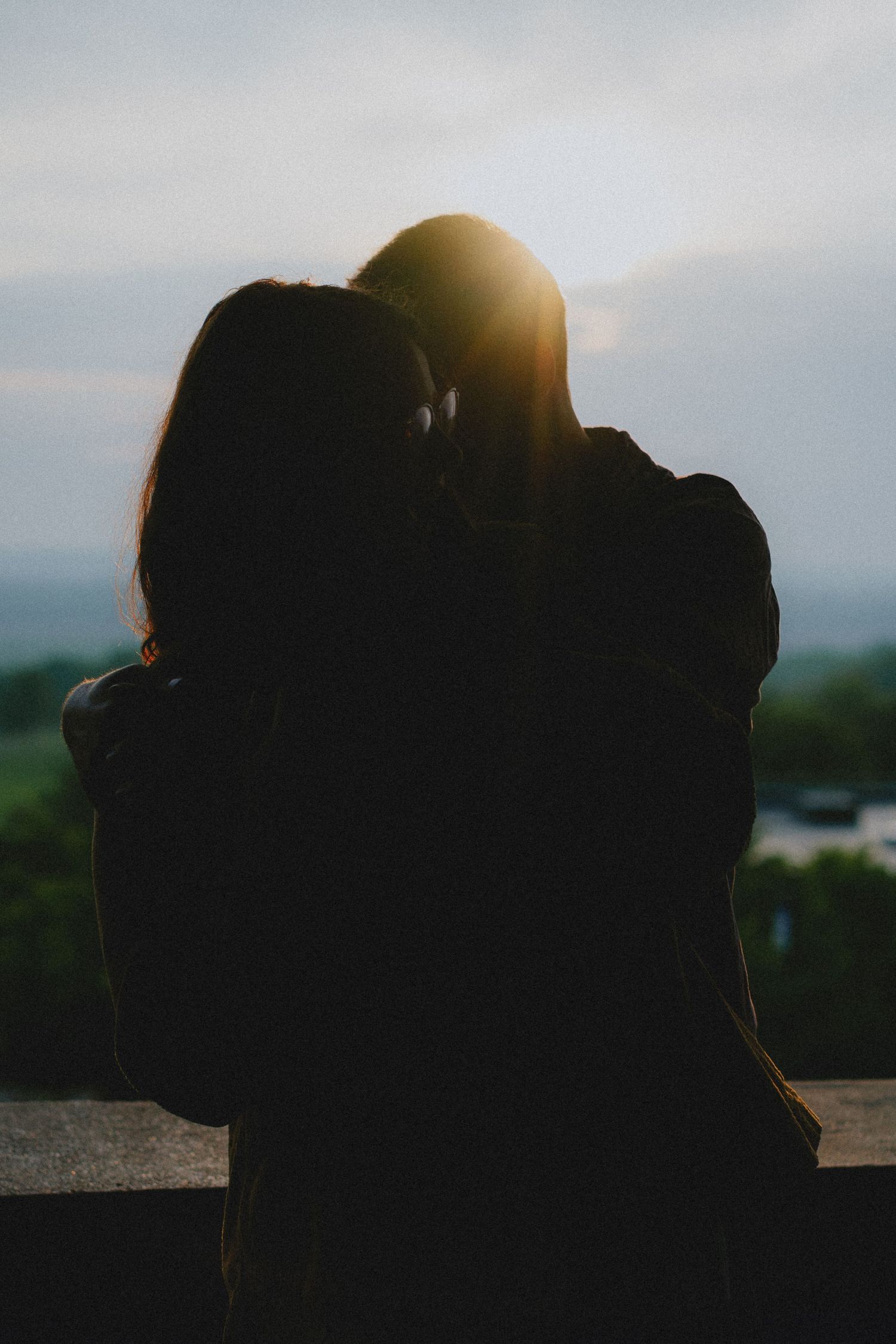 Silhouette of couple embracing at sunset with golden backlight and scenic landscape in background.