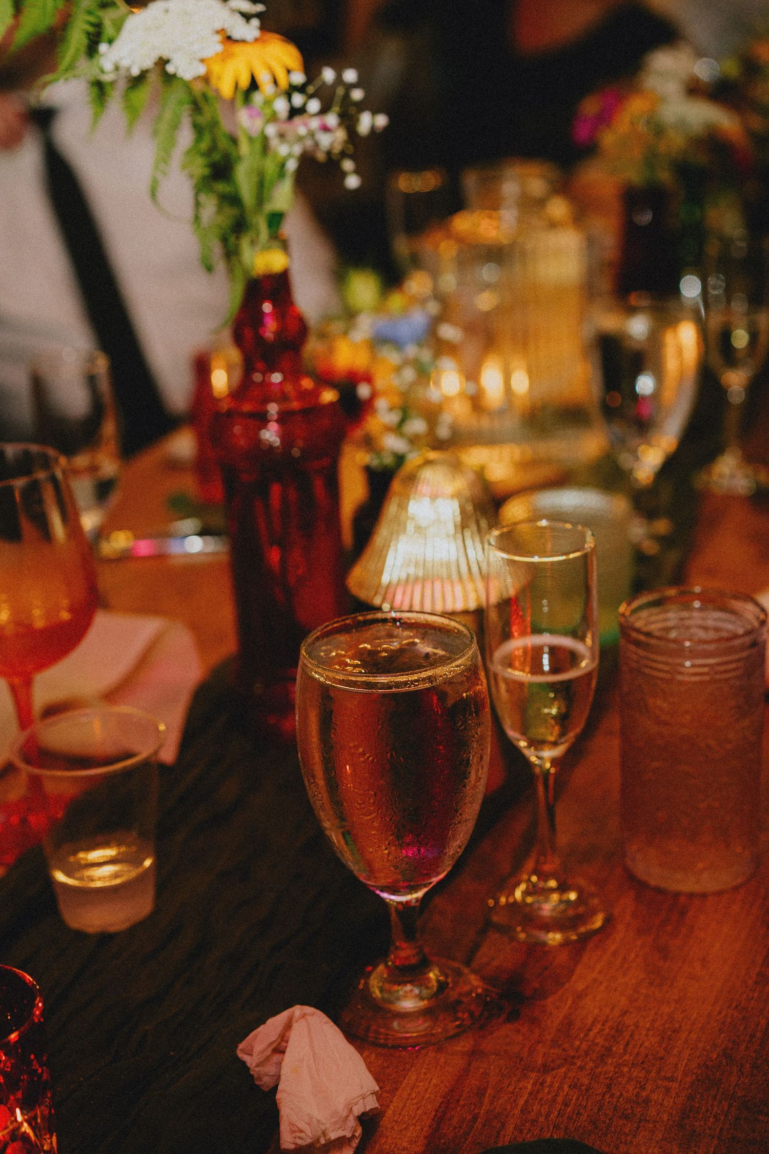 Elegant wedding reception table with champagne flutes, candles, and colorful floral centerpieces on a warm wooden surface.
