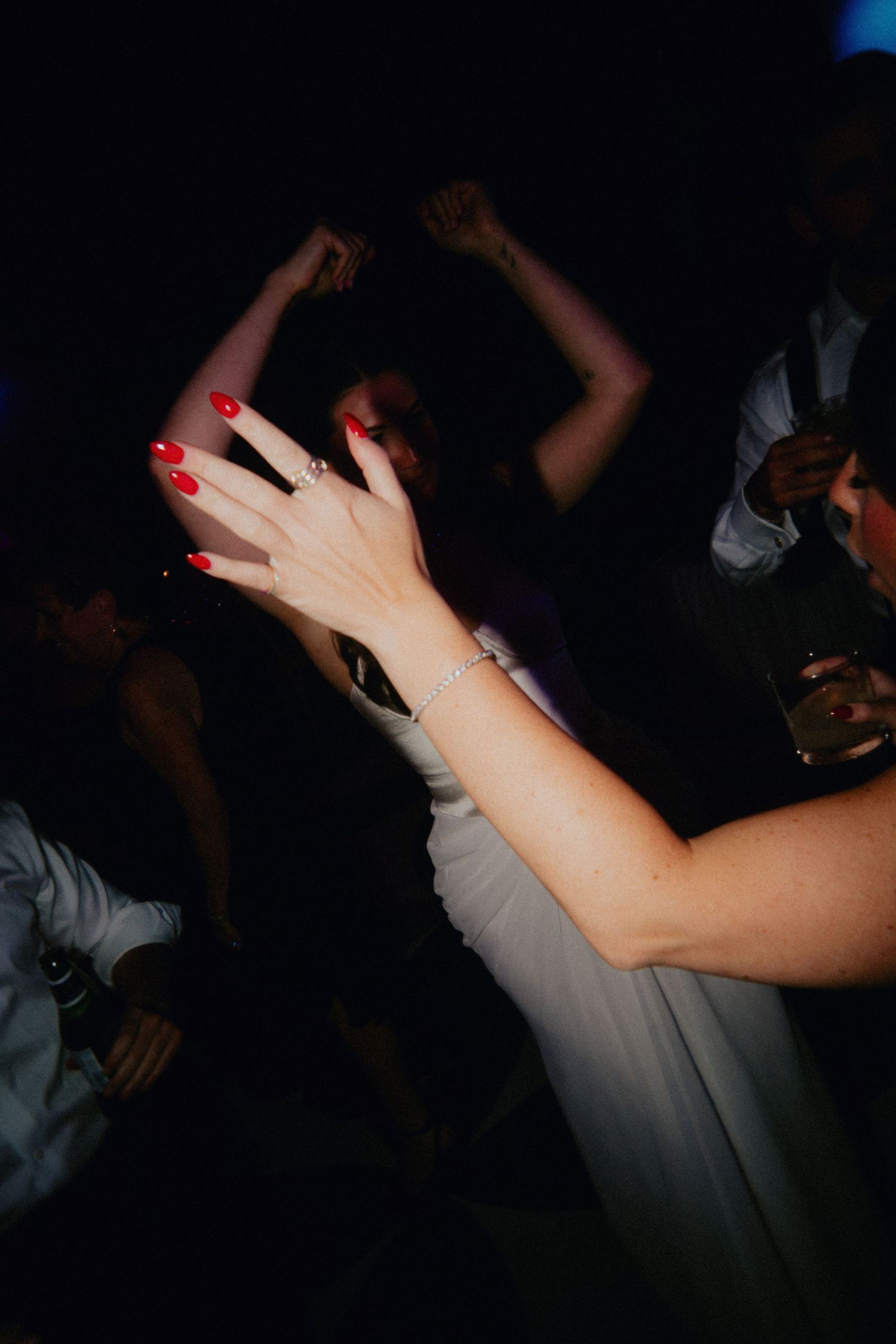 Woman with red nails and bracelet dancing at a dark wedding reception party.