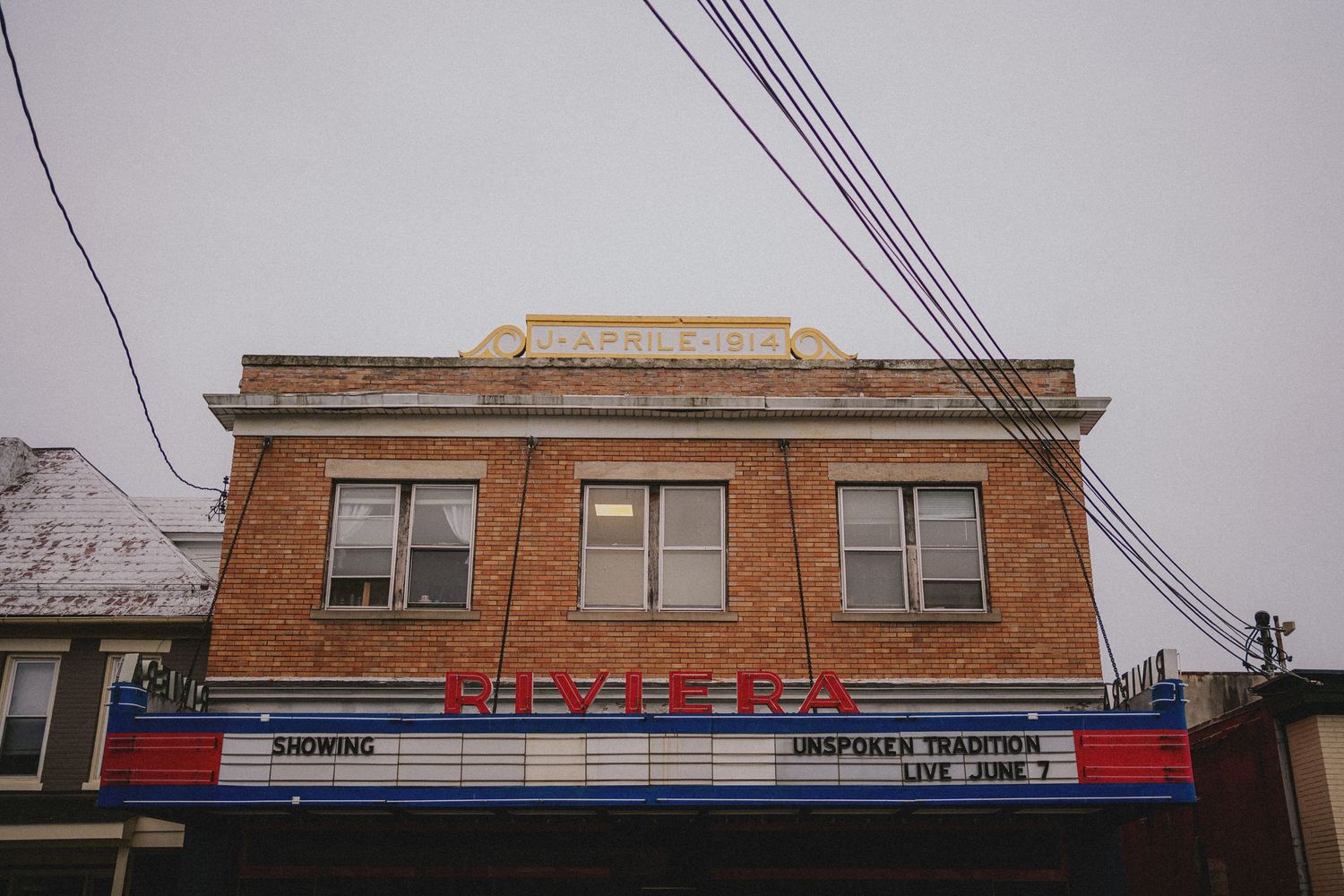 Vintage brick movie theater marquee showing Unspoken Tradition Live June 7 on a cloudy winter day.