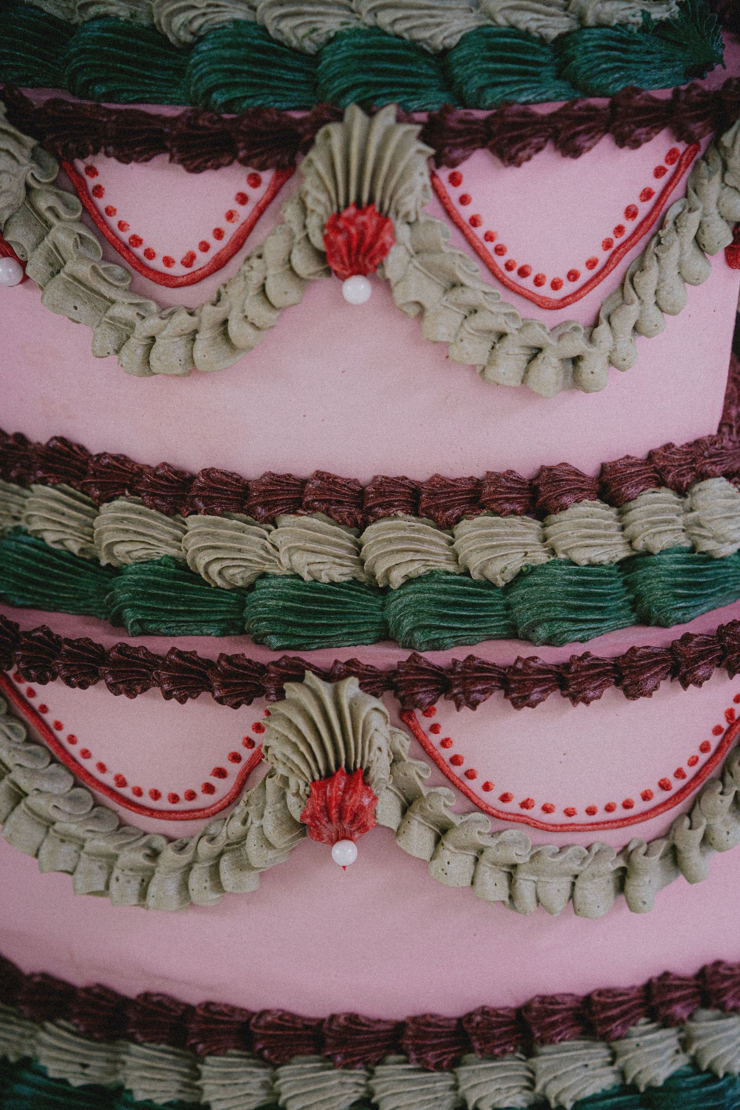 Close-up of a vintage pink layered cake decorated with green, brown, and red buttercream frosting swags and dot details.