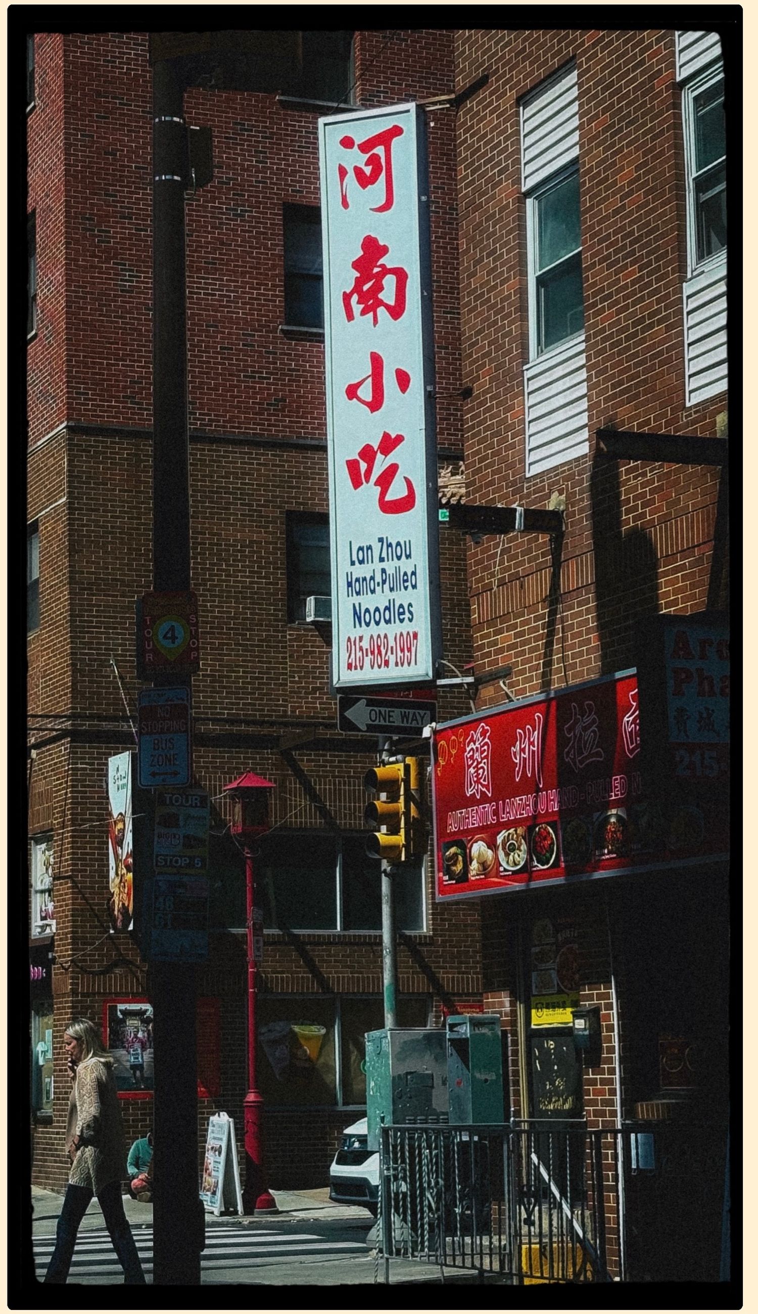 Chinatown street corner featuring Lan Zhou Hand-Pulled Noodles sign with Chinese characters on brick building with traffic lights.