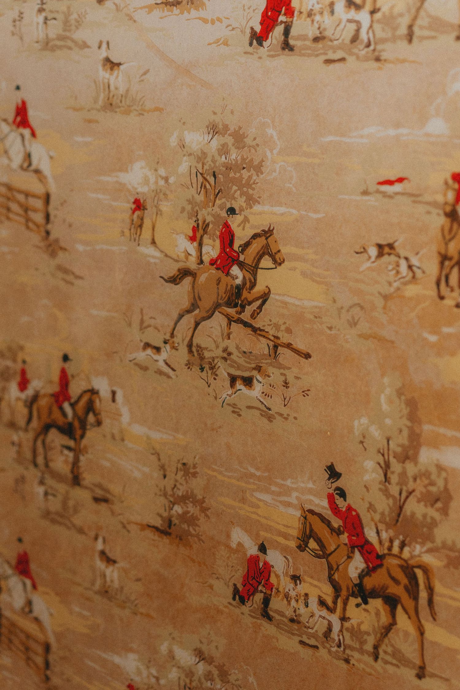 Vintage fox hunting wallpaper featuring riders in red coats on horseback with hounds in a classic equestrian toile pattern.