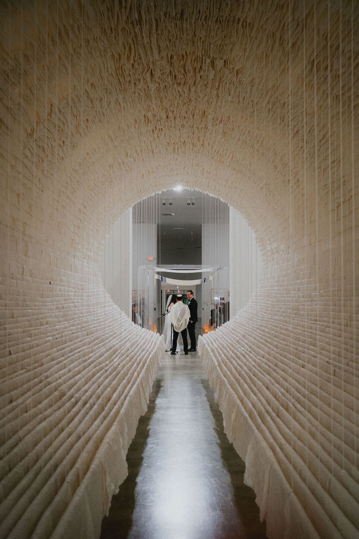 Couple sharing a romantic moment at the end of a stunning white brick tunnel corridor with arched ceiling.