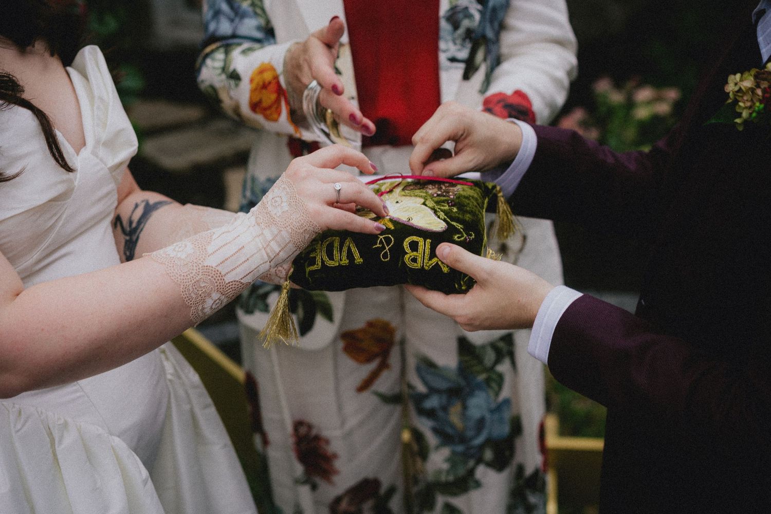 Close-up of wedding ring exchange ceremony with hands holding a decorative pillow outdoors.