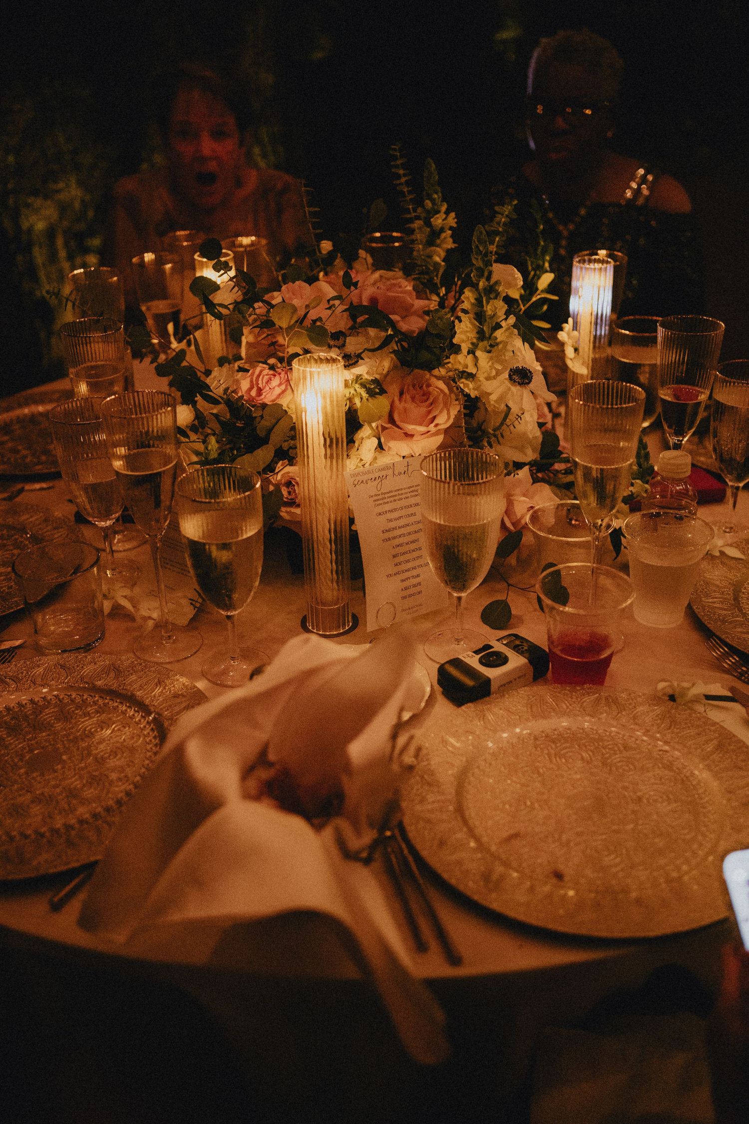 Elegant candlelit wedding reception table with floral centerpiece, champagne flutes, and charger plates in warm romantic lighting.