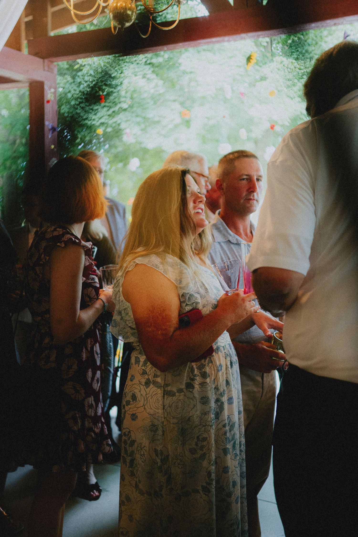 Guests socializing outdoors at a garden party, holding drinks in a lush green setting.