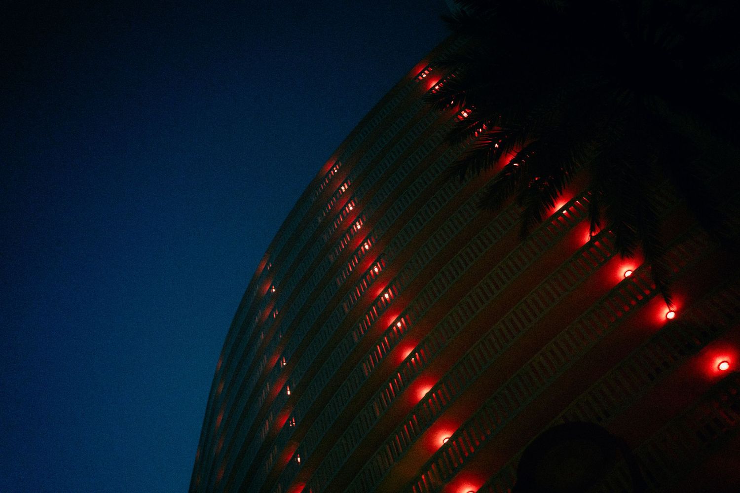 A curved modern building illuminated with red lights against a deep blue night sky.