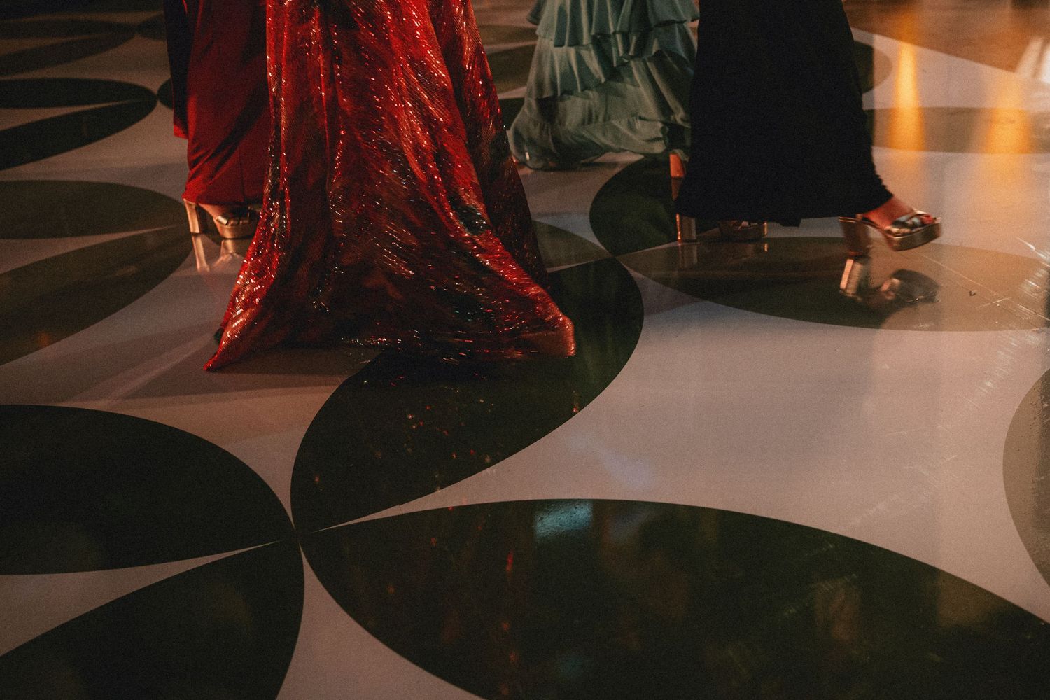 Elegant figures in red sequin and black gowns walking on decorative marble floor with dark swirl patterns.