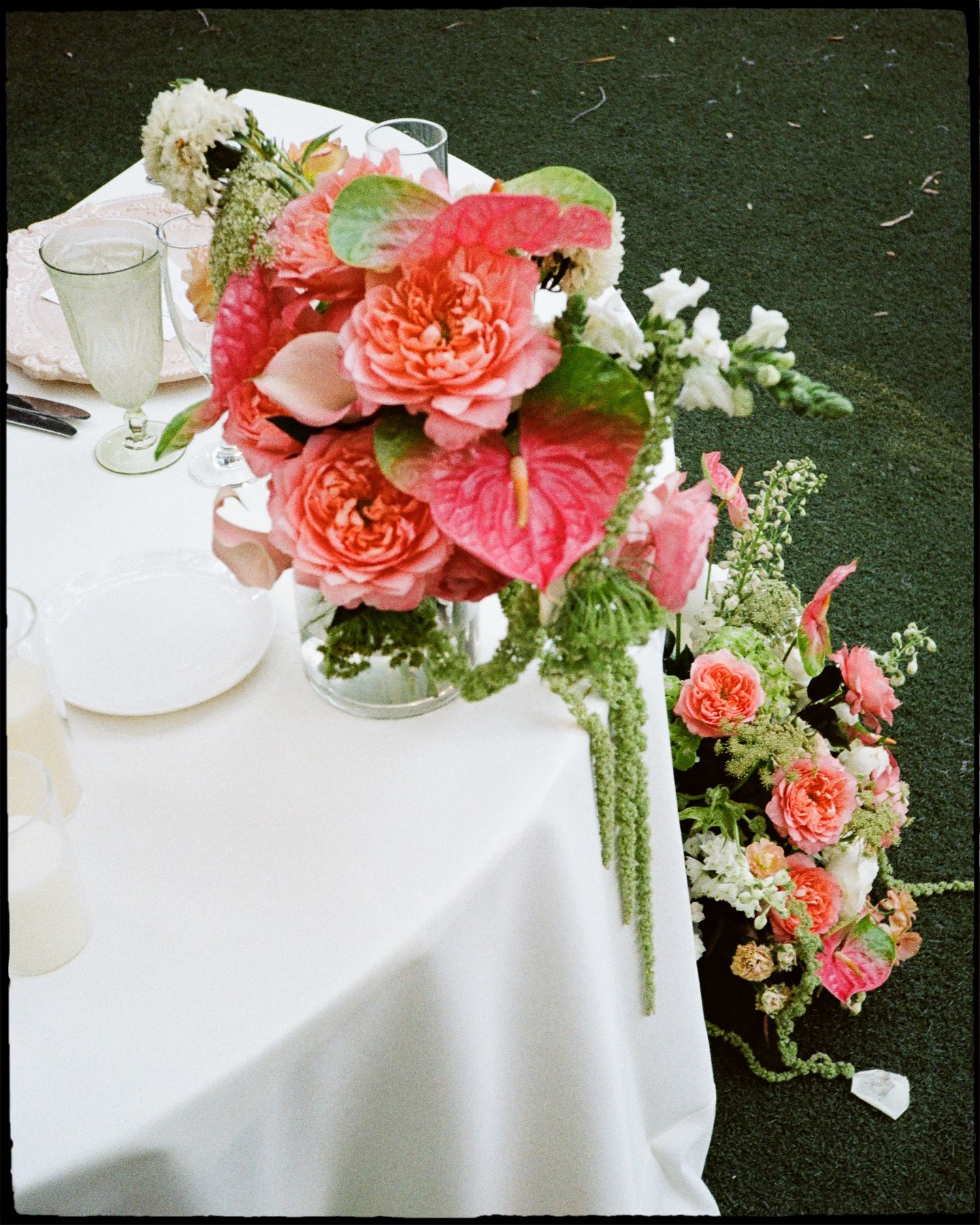 Elegant wedding table with pink coral floral centerpiece featuring roses and anthuriums on white linen tablecloth shot on film.