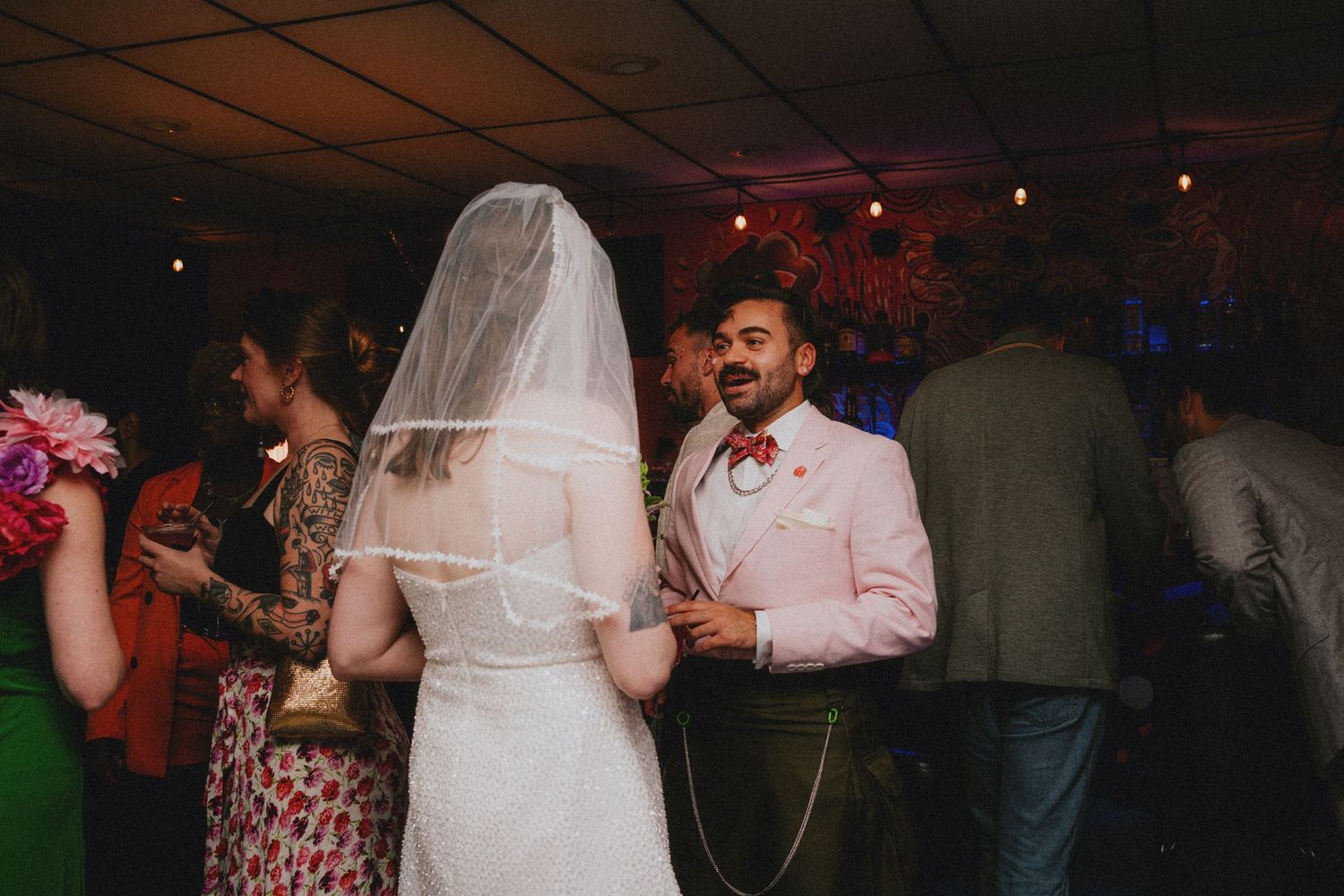 Bride and groom share a dance at their wedding reception, groom wearing pink suit with red boutonniere.