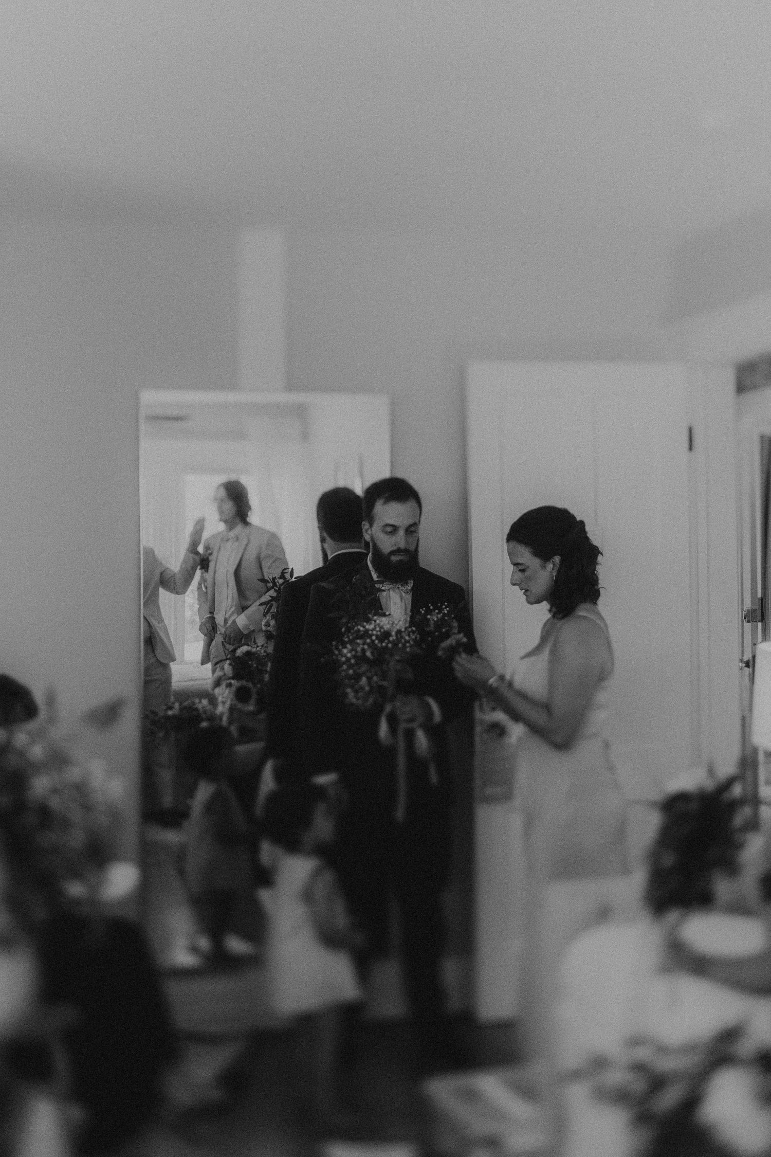 Black and white wedding photo of bride and groom with bouquet, mirror reflection visible in elegant indoor setting.