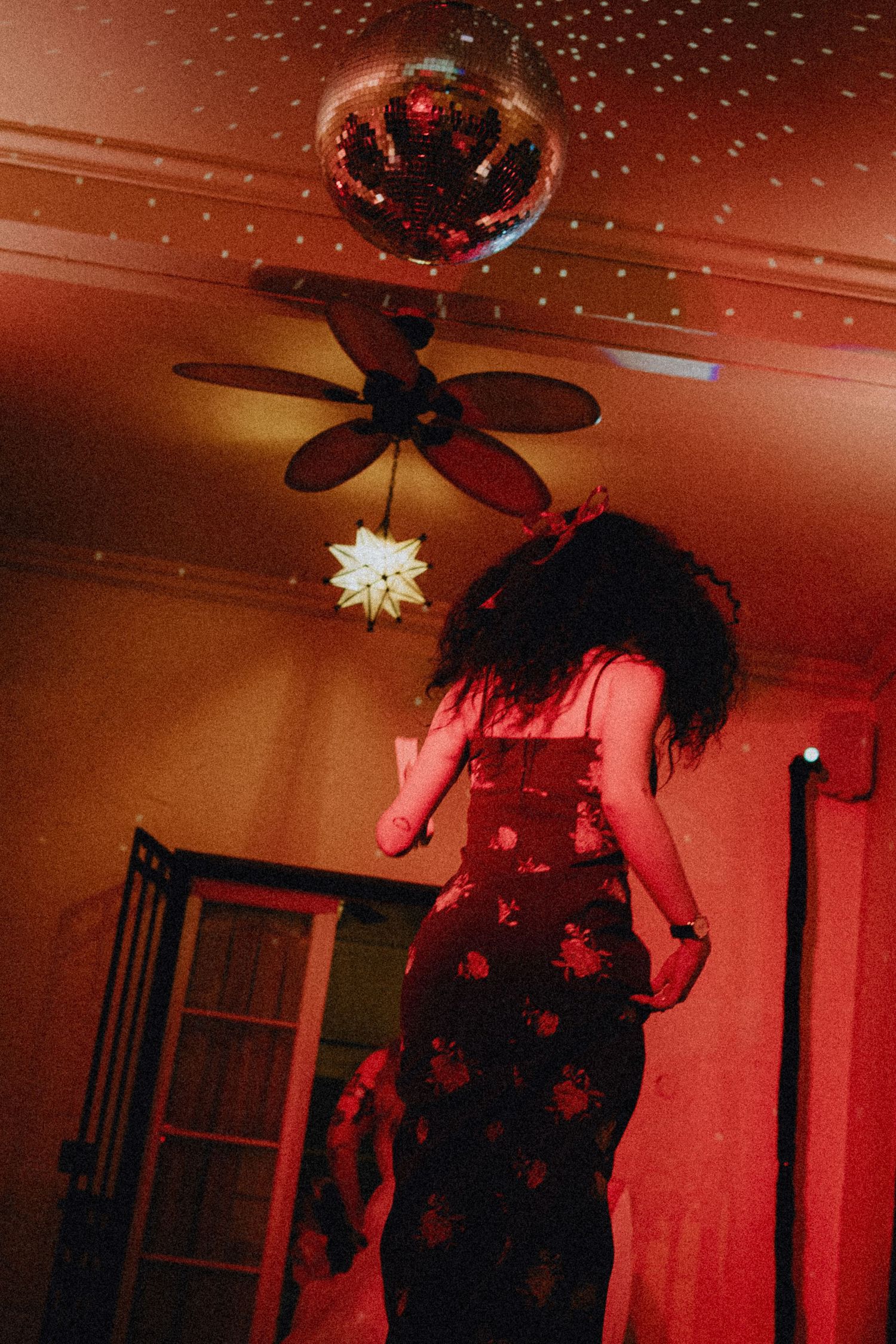 Woman in floral dress dancing under a disco ball with red ambient lighting and ceiling fan.