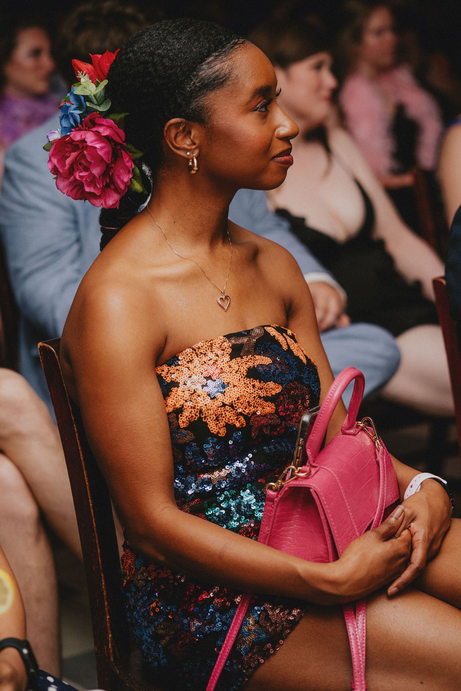 Woman in sequined strapless dress with pink flower hair accessory holding pink handbag at an event.