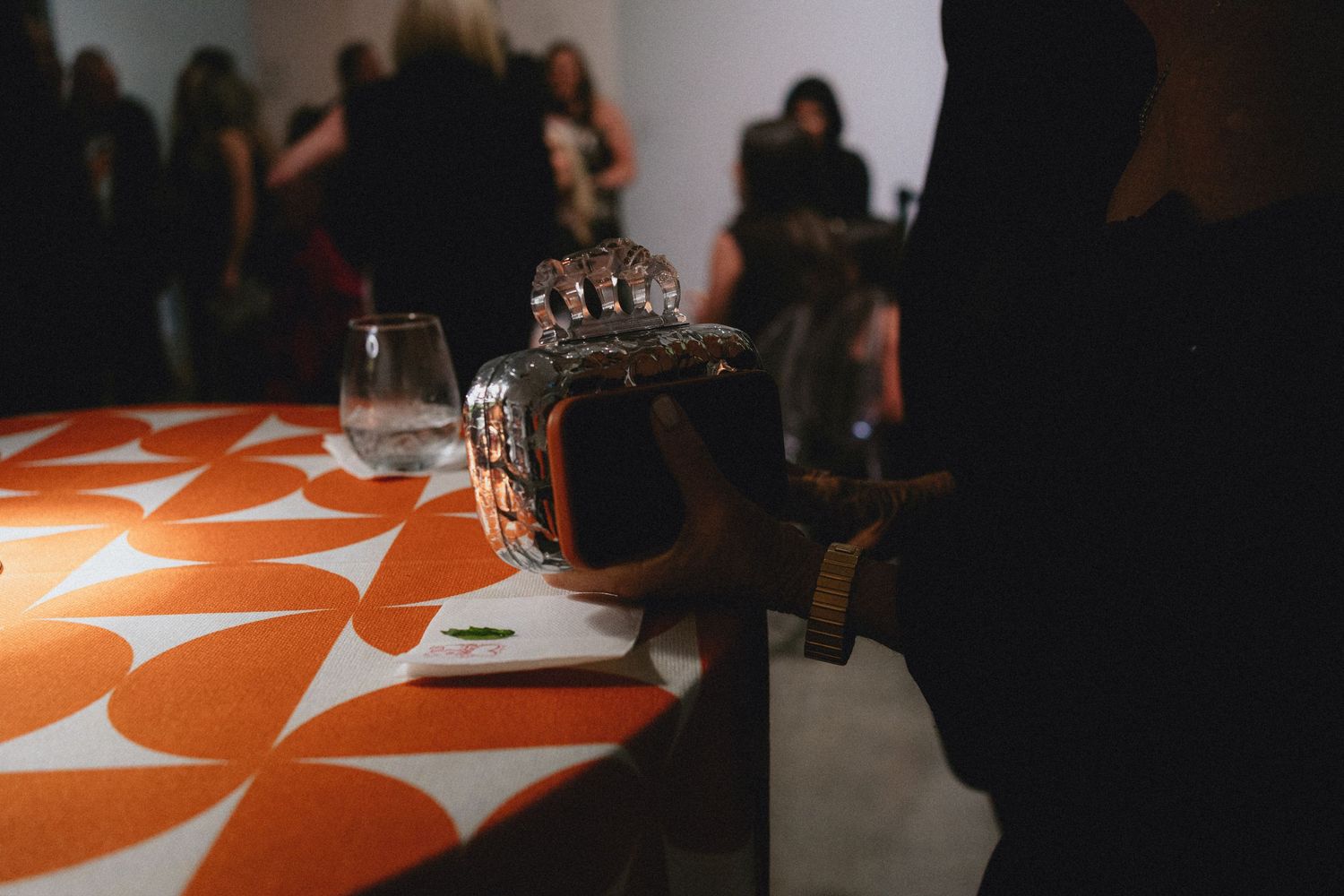 A decorative orange geometric tablecloth with a crystal vase and glass at an indoor event gathering.