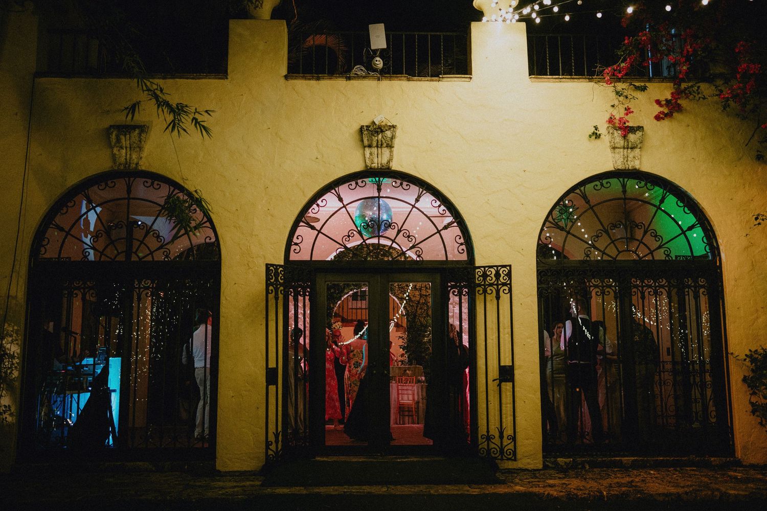 Elegant venue entrance with ornate iron doors, colorful stained glass windows, and warm lighting at night.