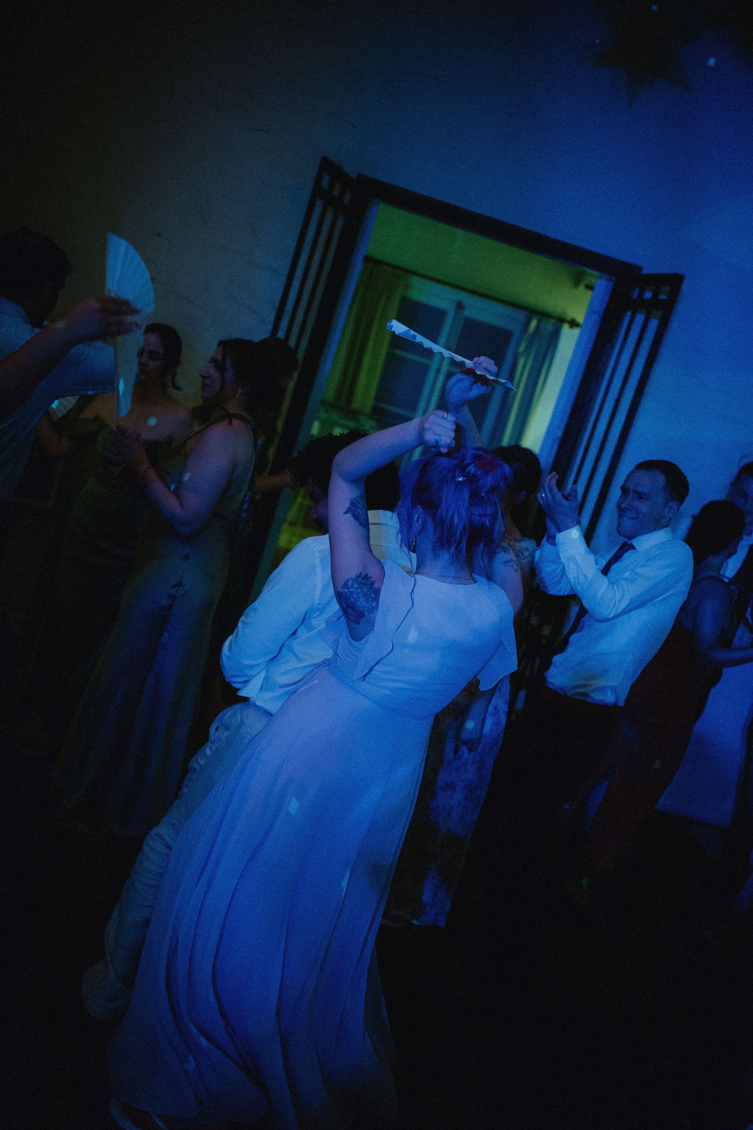 Bride and groom dancing with guests under blue lights at a lively wedding reception party.