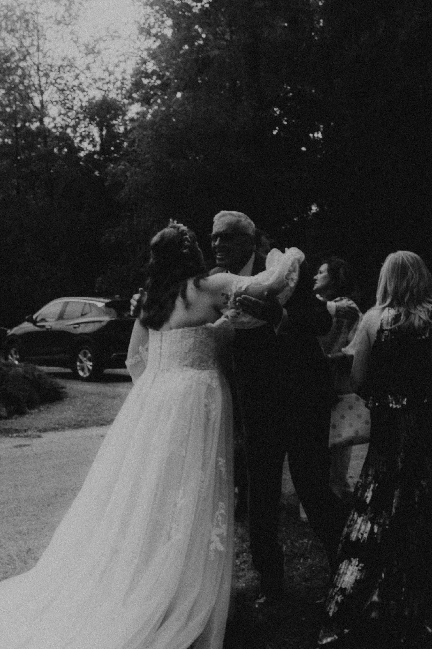 Black and white photo of a bride dancing with her father at an outdoor wedding reception surrounded by guests.