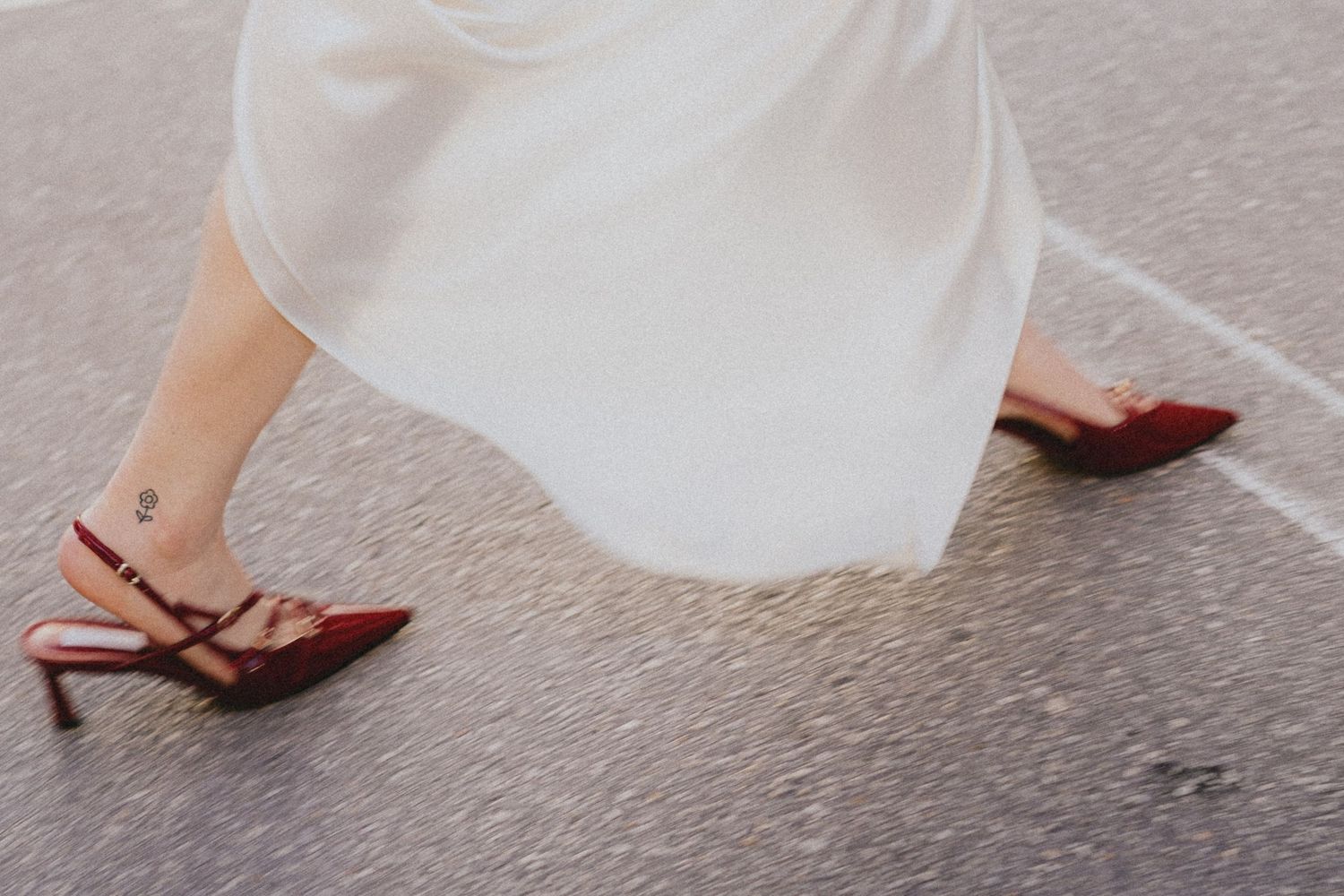 Bride walking in red stiletto heels with a white wedding dress on a gray pavement.