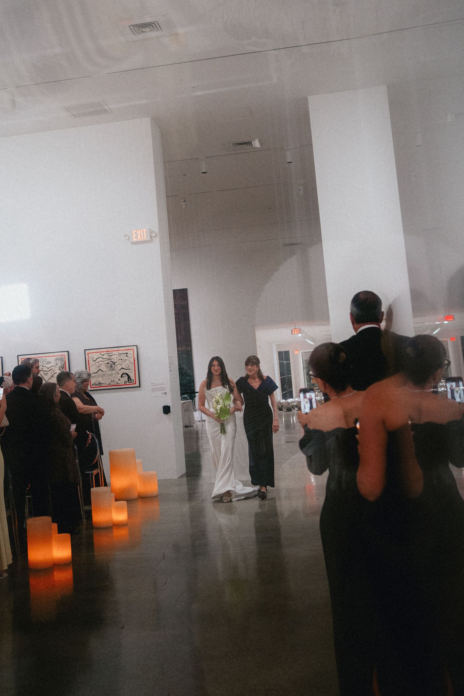 Bride walks down the aisle in a modern art gallery wedding venue with glowing candles lining the path.