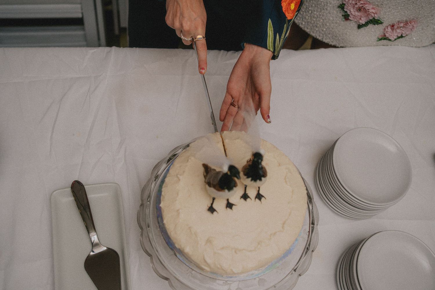 Person cutting a white frosted cake decorated with black bird figurines at a celebration event.