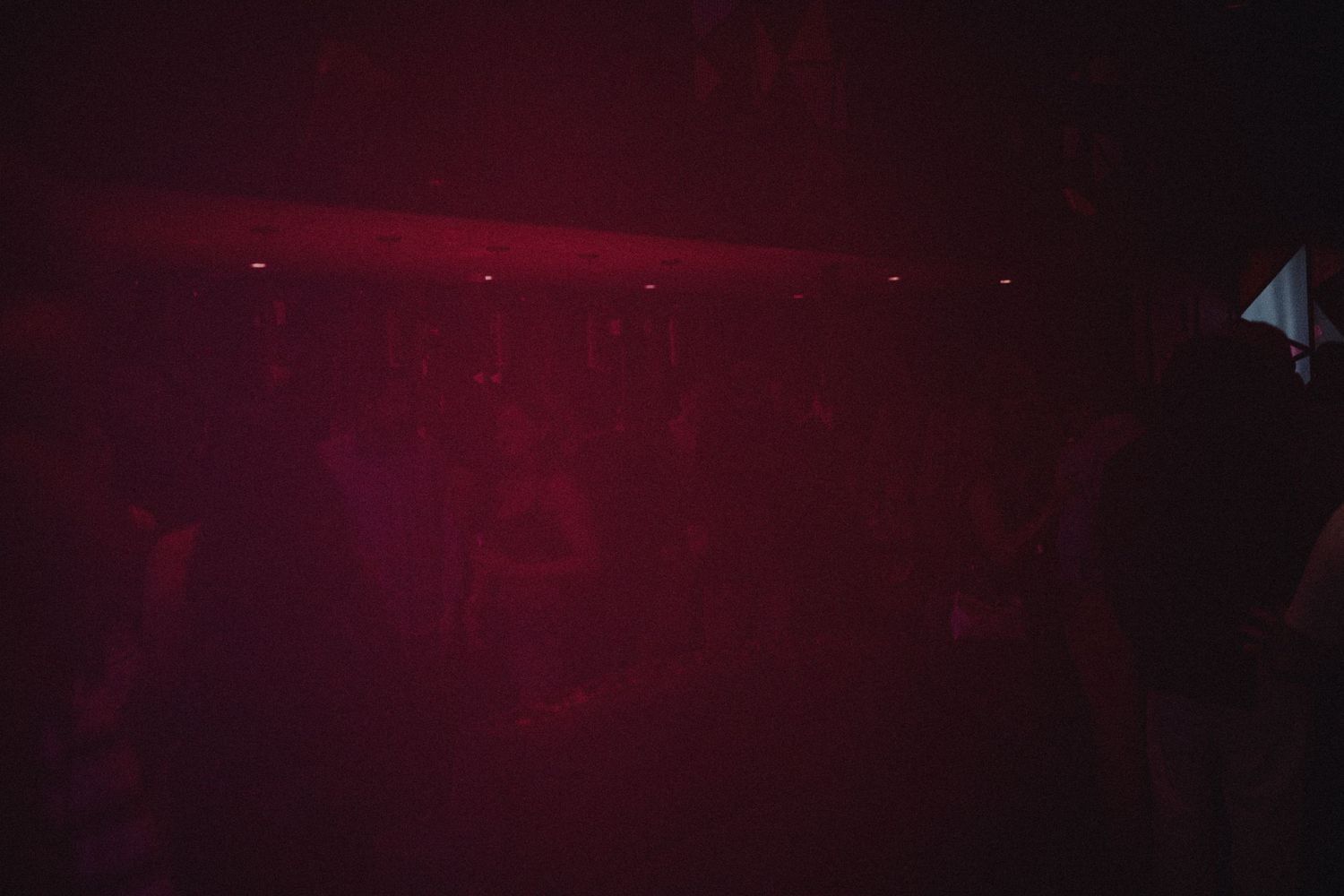 Dark red-lit nightclub interior with atmospheric haze and stage lighting creating a moody ambiance.