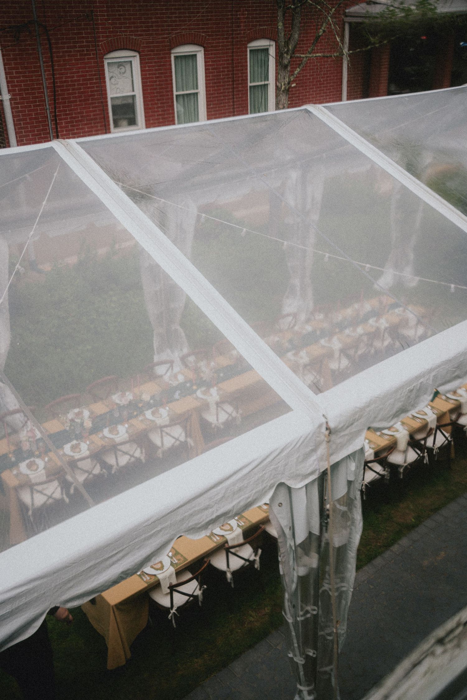 Aerial view of a clear wedding reception tent with long wooden tables and chairs set up on a green lawn.