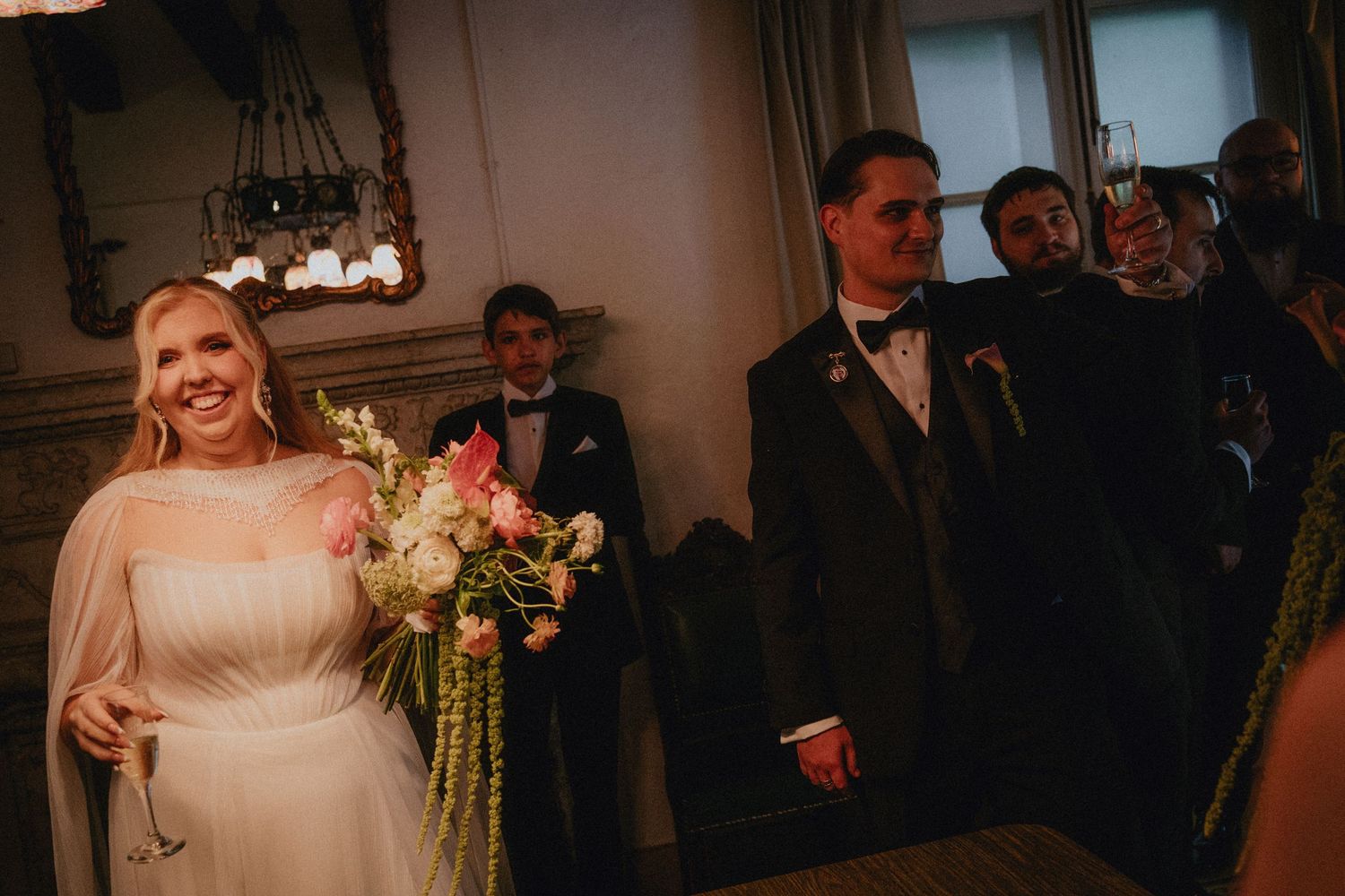 Smiling bride holding a colorful bouquet stands beside groom in elegant indoor wedding ceremony setting.