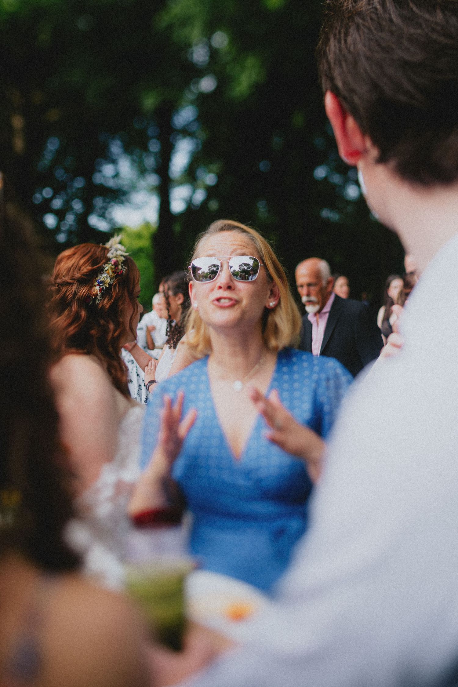 Woman in blue dress and mirrored sunglasses socializing at an outdoor wedding reception.