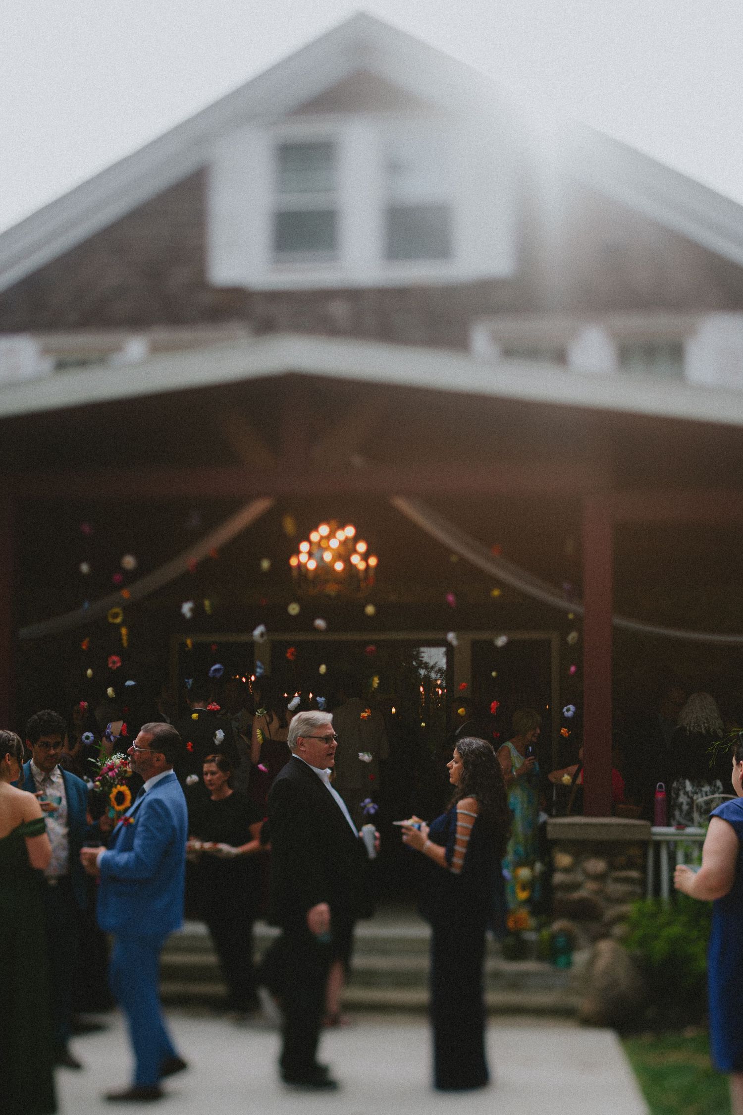 Guests dancing outdoors at a rustic wedding reception venue at dusk with string lights and colorful decorations.