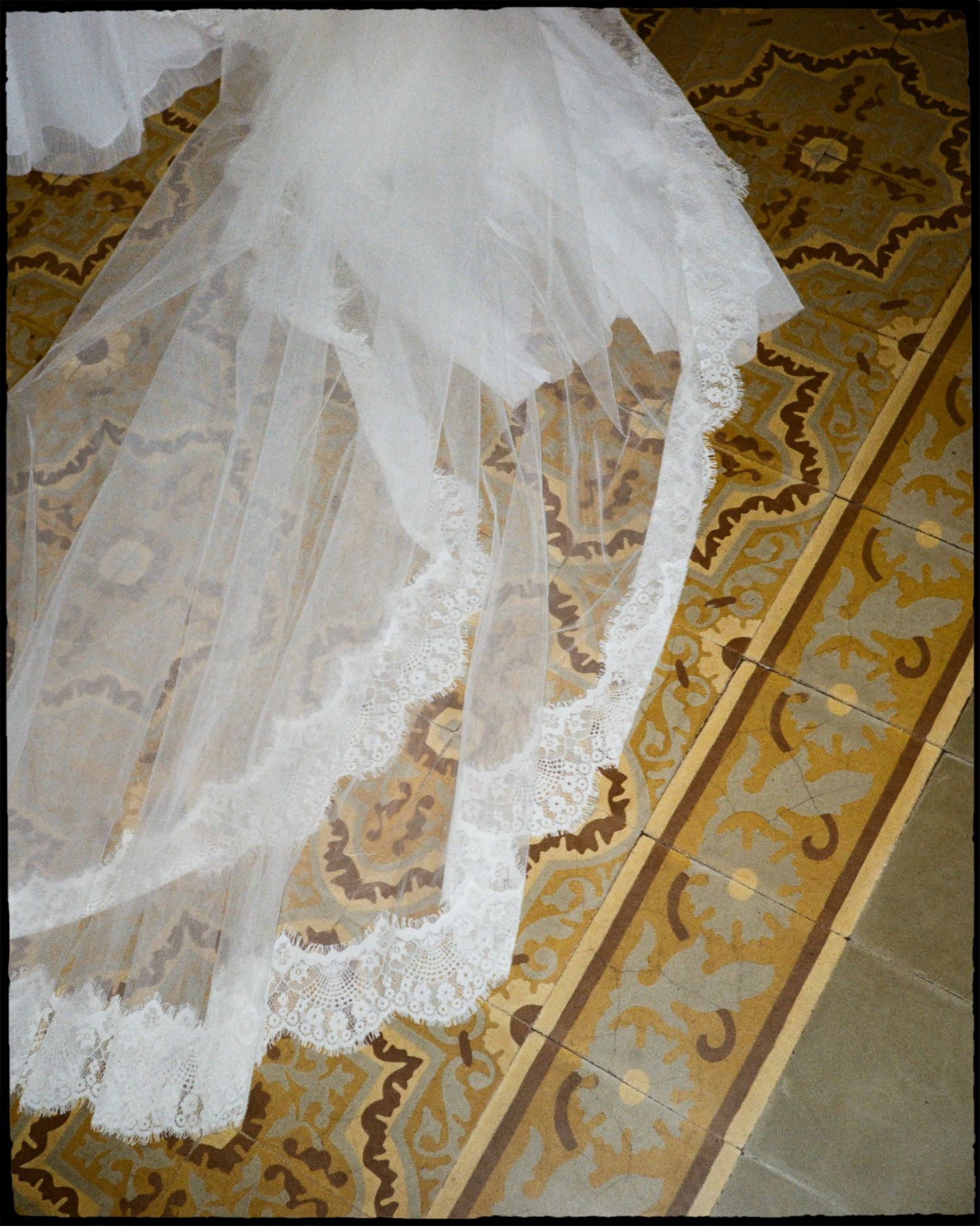White lace wedding veil draped over ornate gold and brown patterned tile floor shot on film.