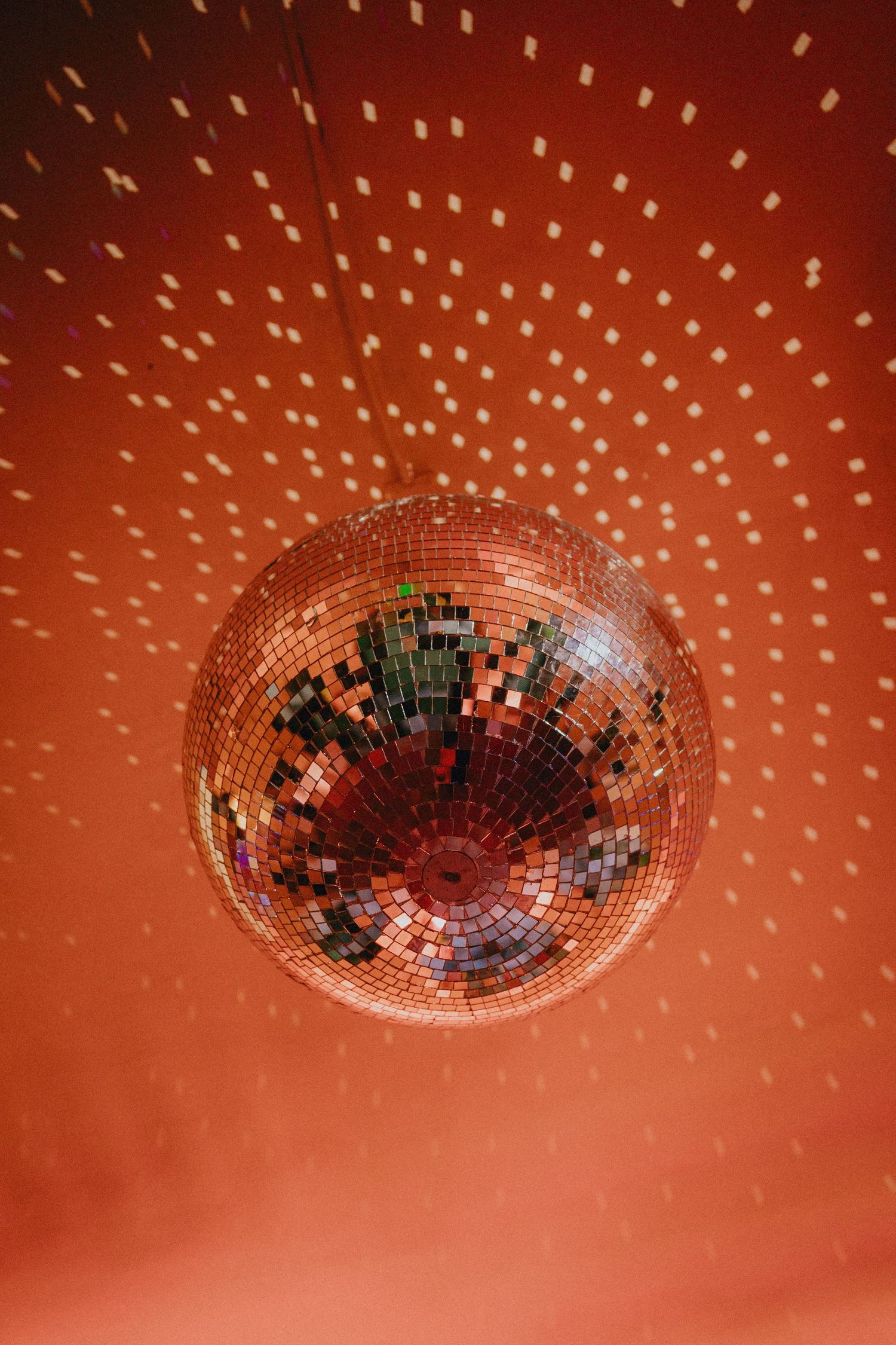 A glittering disco ball hanging from a red-lit ceiling, casting shimmering light reflections across the room.