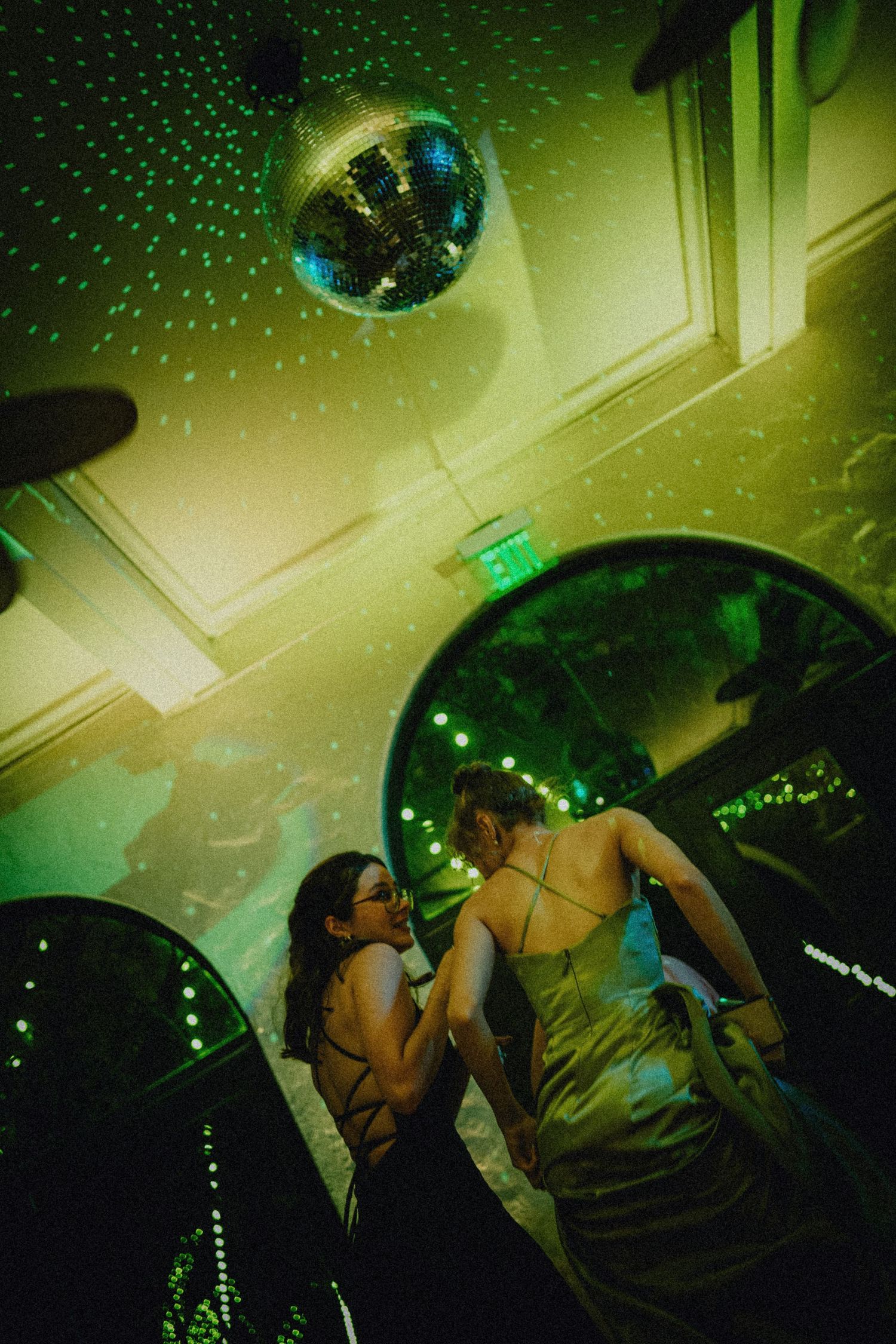 Two women dancing under a disco ball with green laser lights at a glamorous evening event.