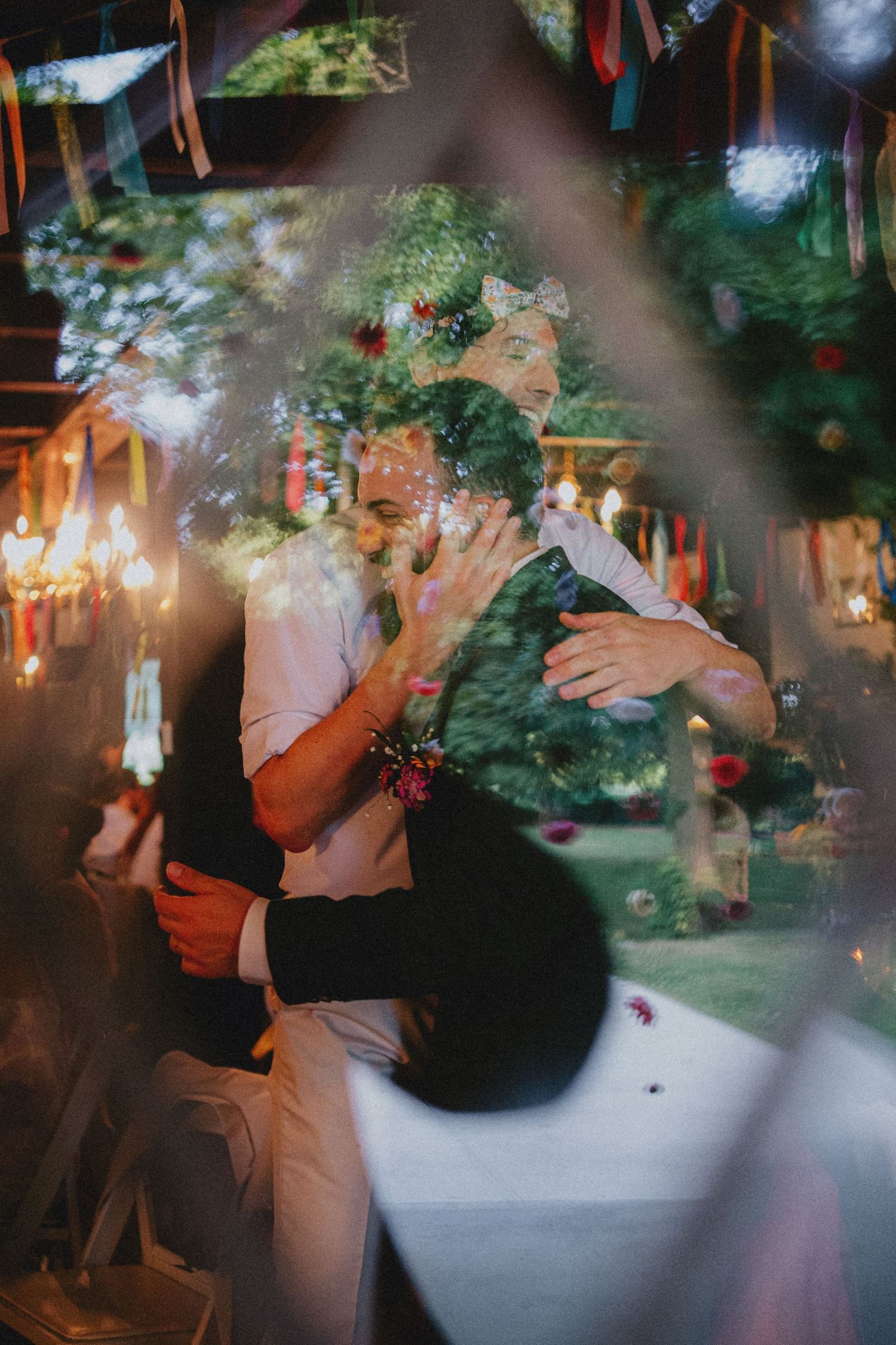 Couple sharing a romantic kiss at a colorful outdoor wedding celebration with festive decorations and warm lighting.