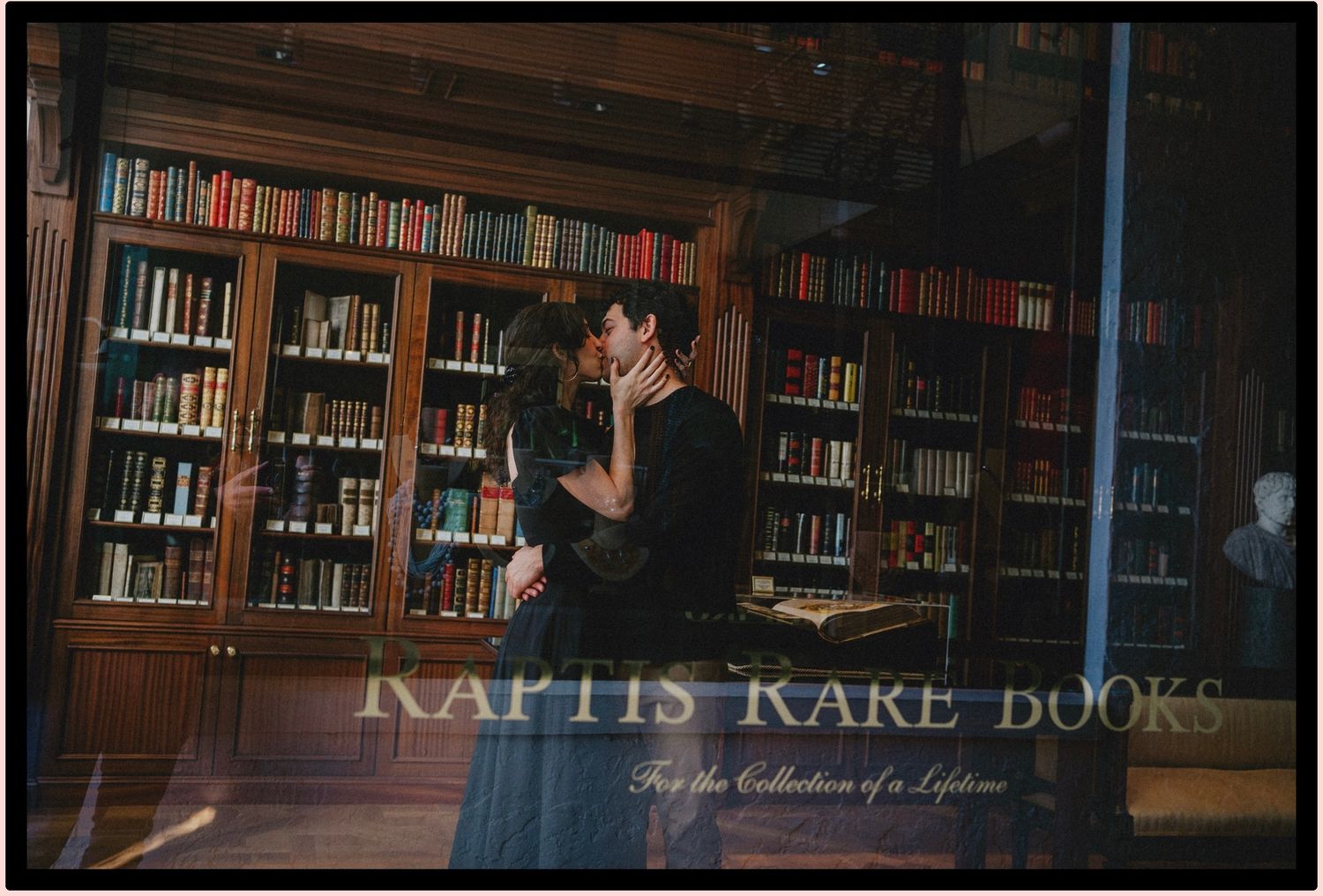 Couple sharing a romantic kiss in a warmly lit library at Kaptis Kake Books, surrounded by shelves of colorful books.