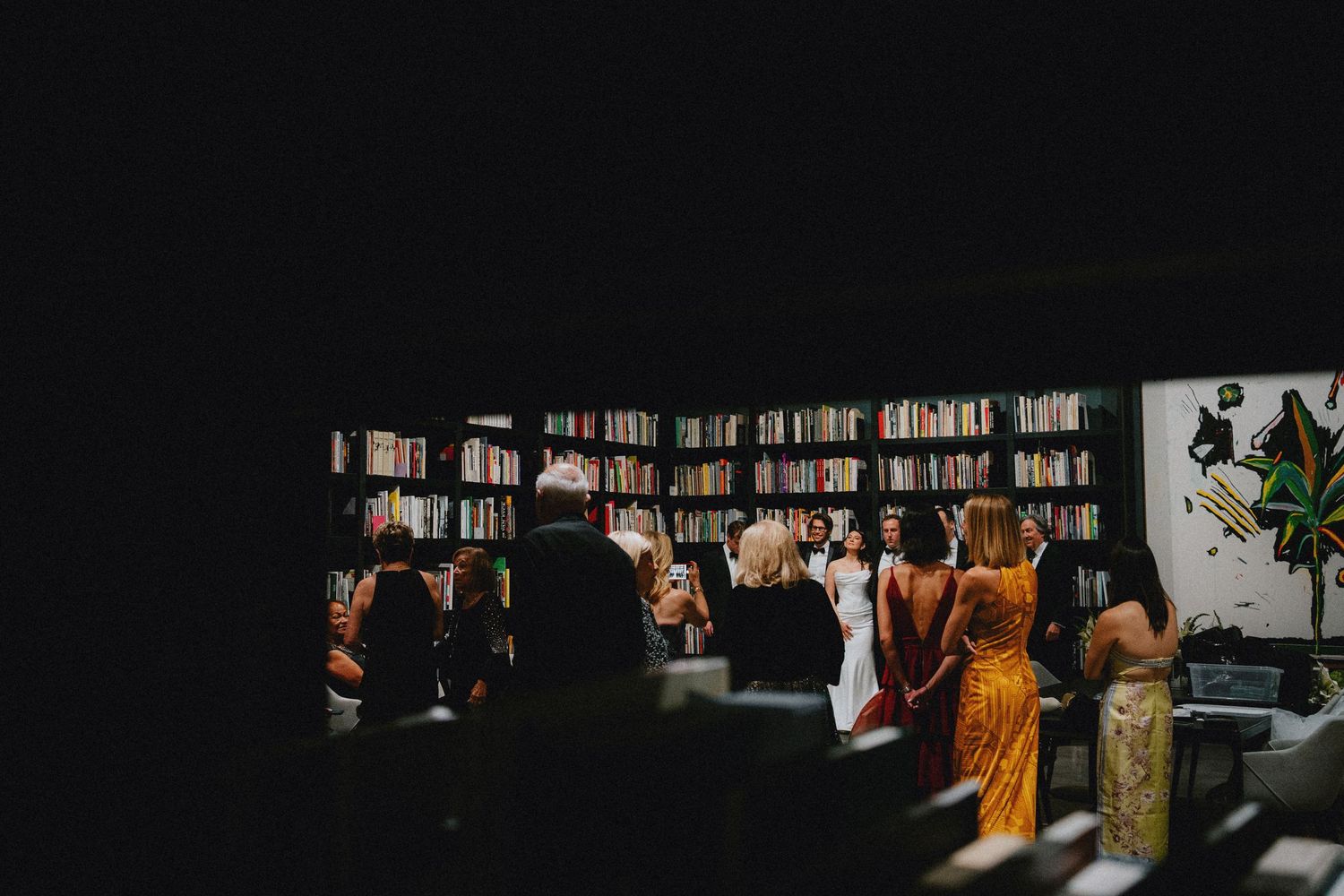 Guests gather in a dimly lit bookstore library venue during an elegant wedding ceremony celebration.