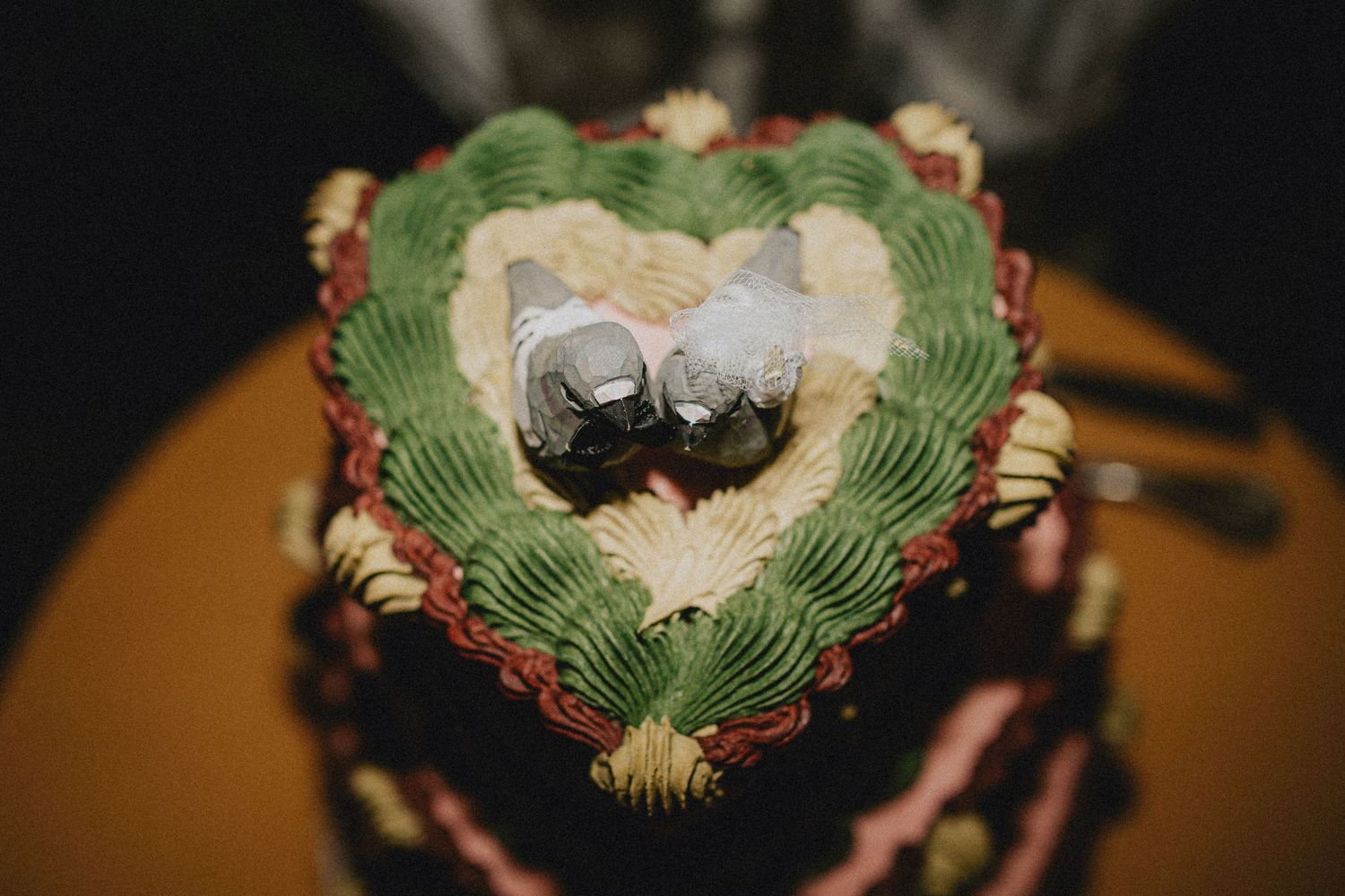 Heart-shaped wedding cake with green and pink frosting topped with two silver bird cake toppers.
