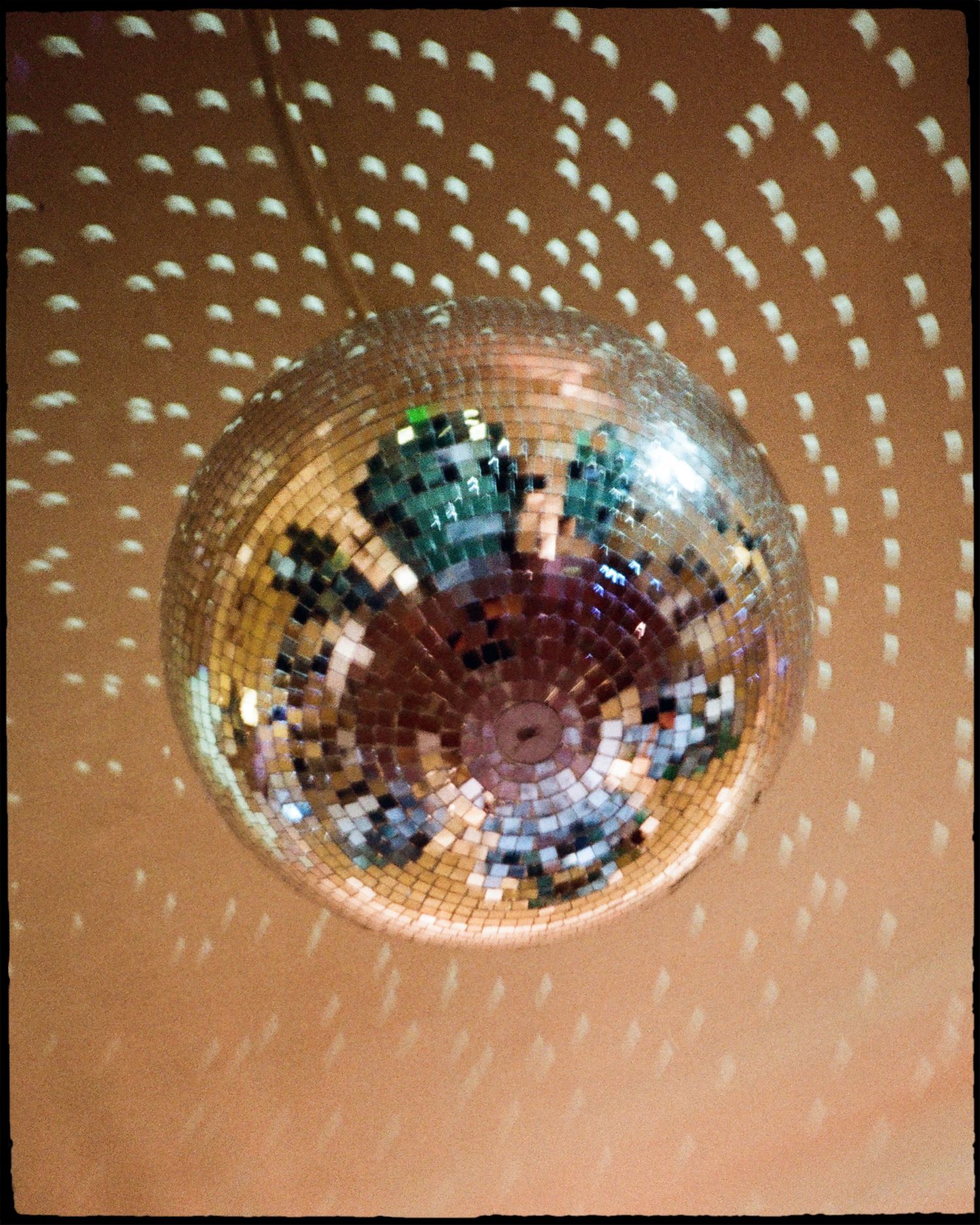 A shimmering disco ball hanging from a ceiling, reflecting light patterns across a the ceiling and walls shot on film.