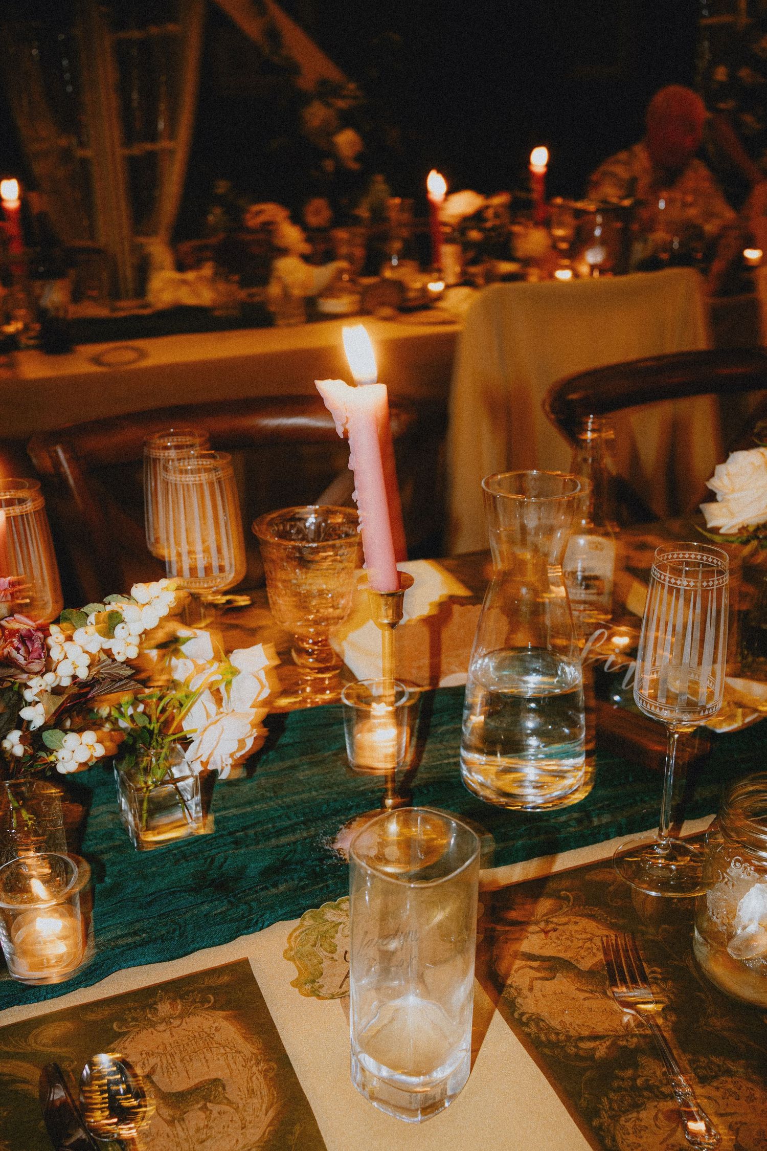 Elegant candlelit dinner table with glassware, pink taper candle, floral centerpiece, and map placemats at a romantic evening event.