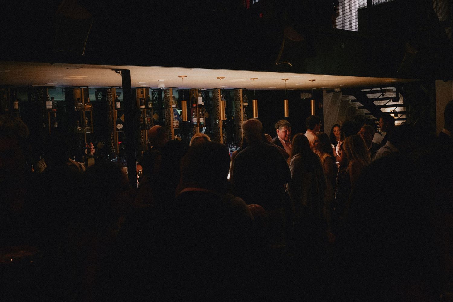 Guests mingle in a dimly lit venue during an evening social event with warm candlelight ambiance.