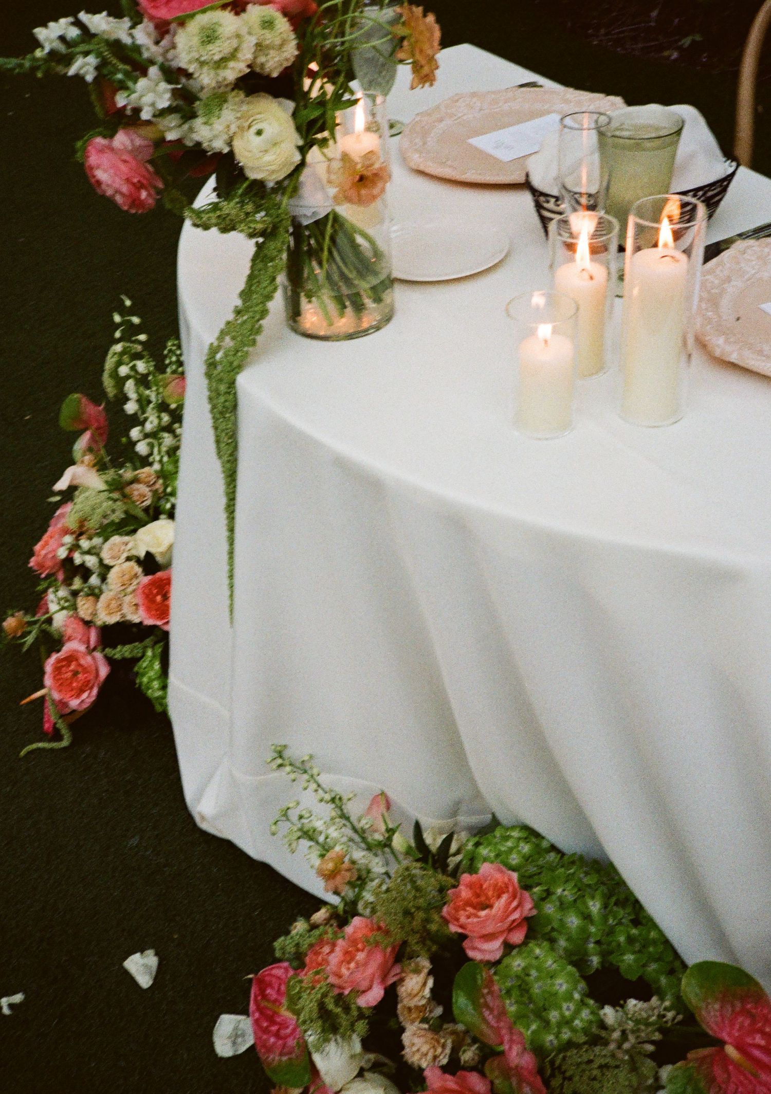 Elegant wedding sweetheart table with white linen, pillar candles, and lush pink floral arrangements cascading to the floor.